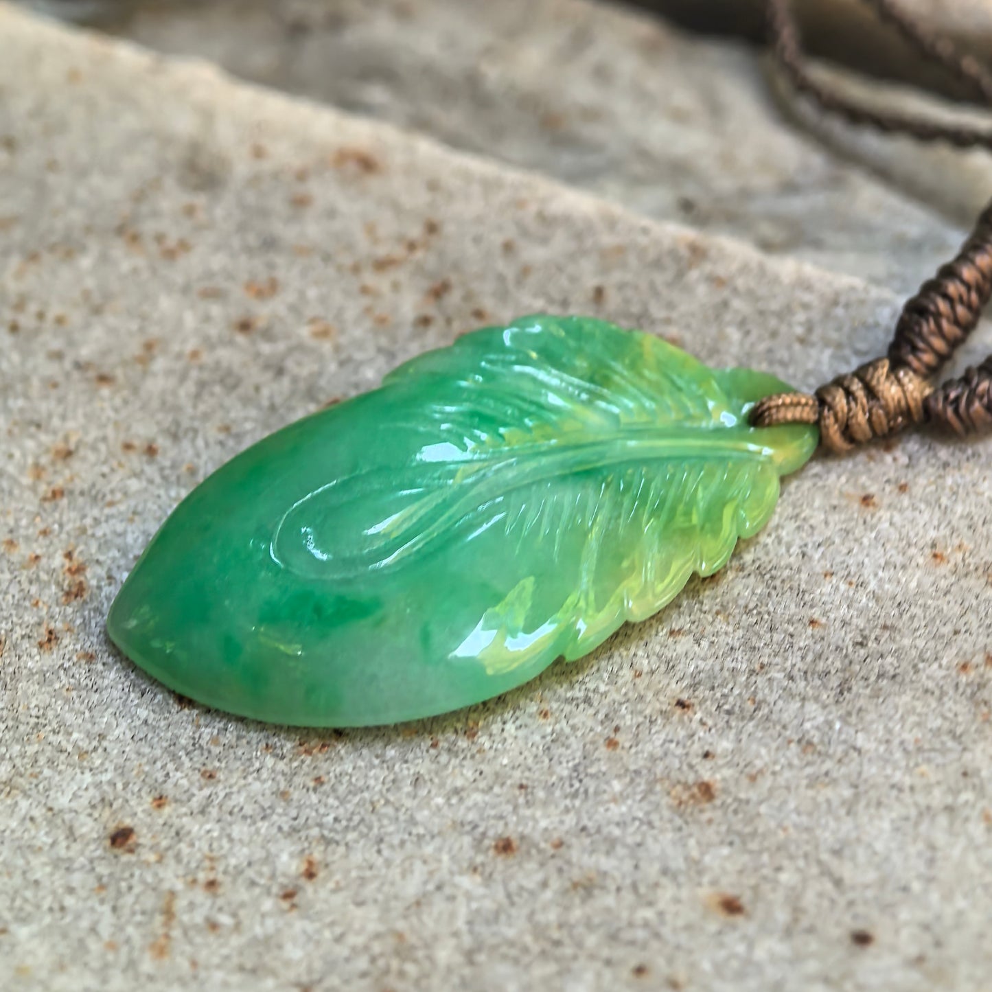 Close-up of carved jadeite leaf pendant showing light green tones and detailed vein carving.