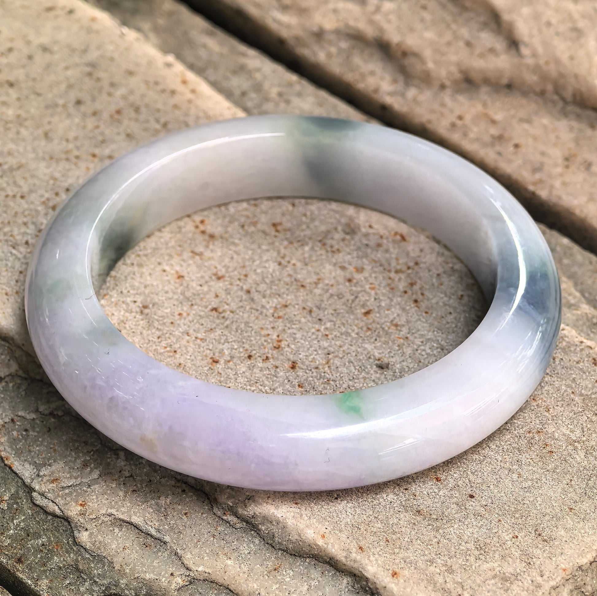 Side view of glutinous lavender denim blue D-shape jadeite bangle on stone background.