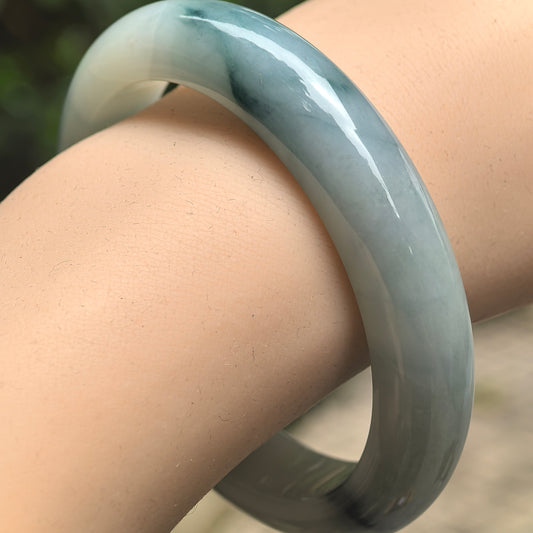 Natural Grade-A pale green jadeite D-shape bangle with deep green floating color worn on the wrist.