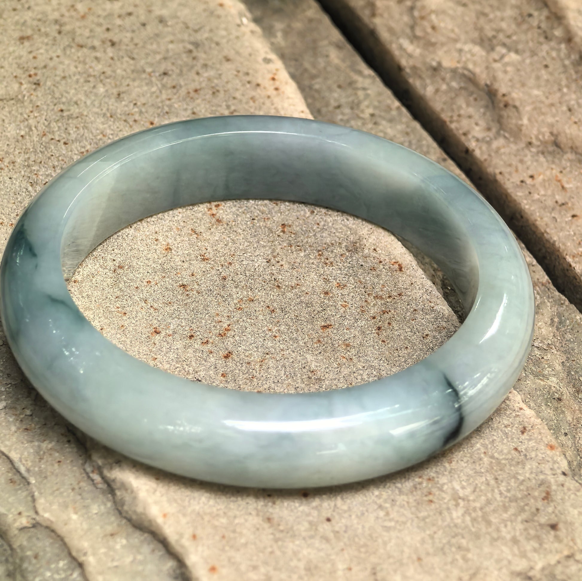 Side view of glutinous pale green D-shape jadeite bangle on stone background.