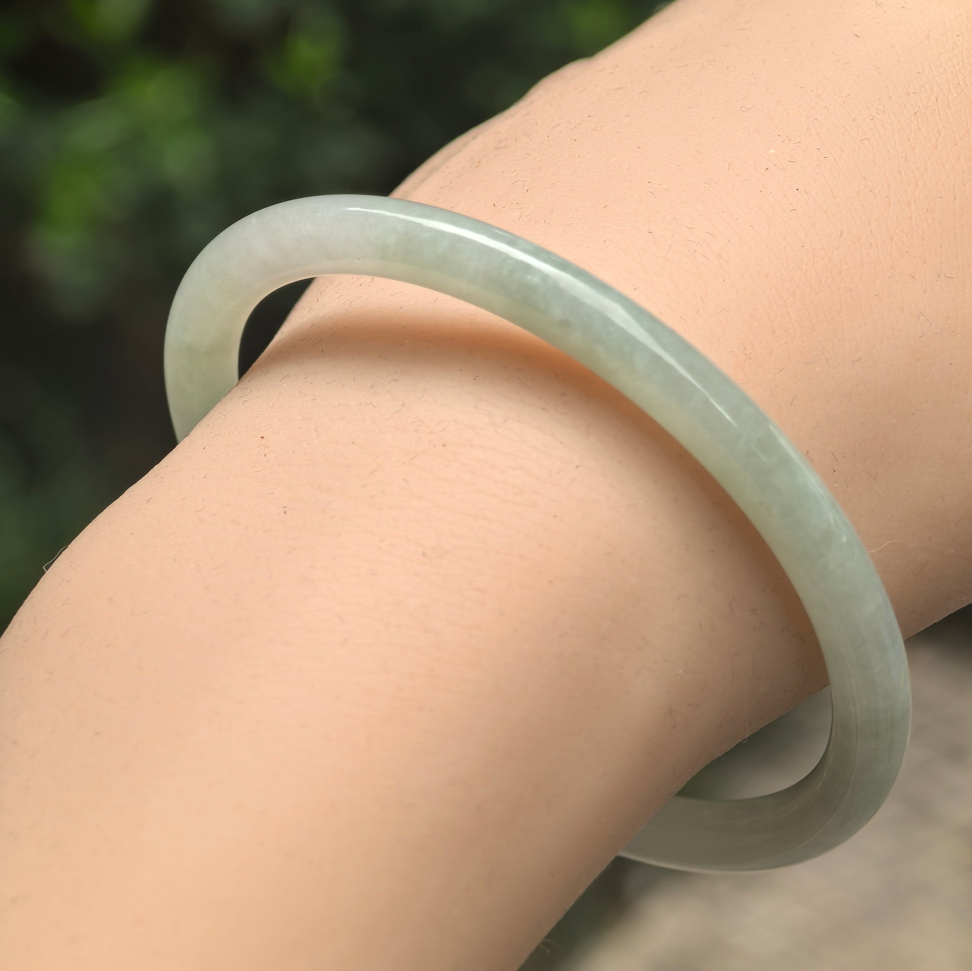 Natural Grade-A glutinous light green slim round-bar jadeite bangle worn on wrist.