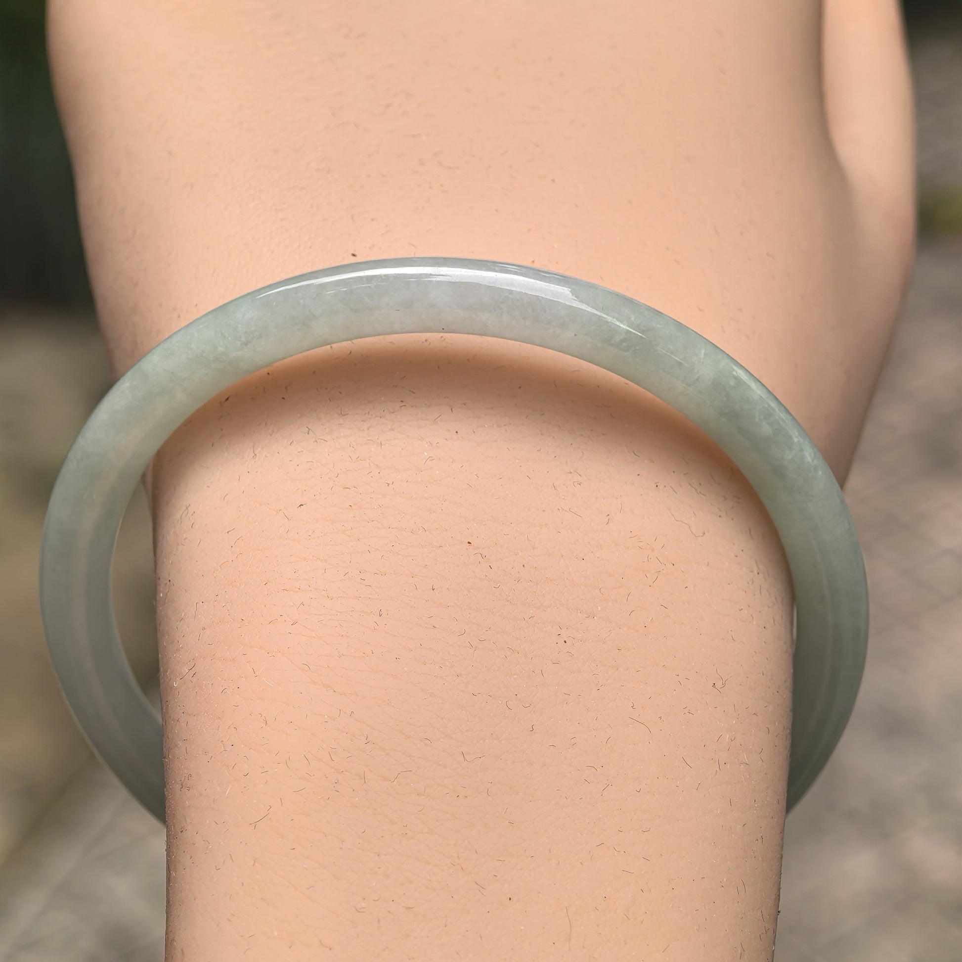 Close-up of light green jadeite bangle showing smooth slim round-bar shape.