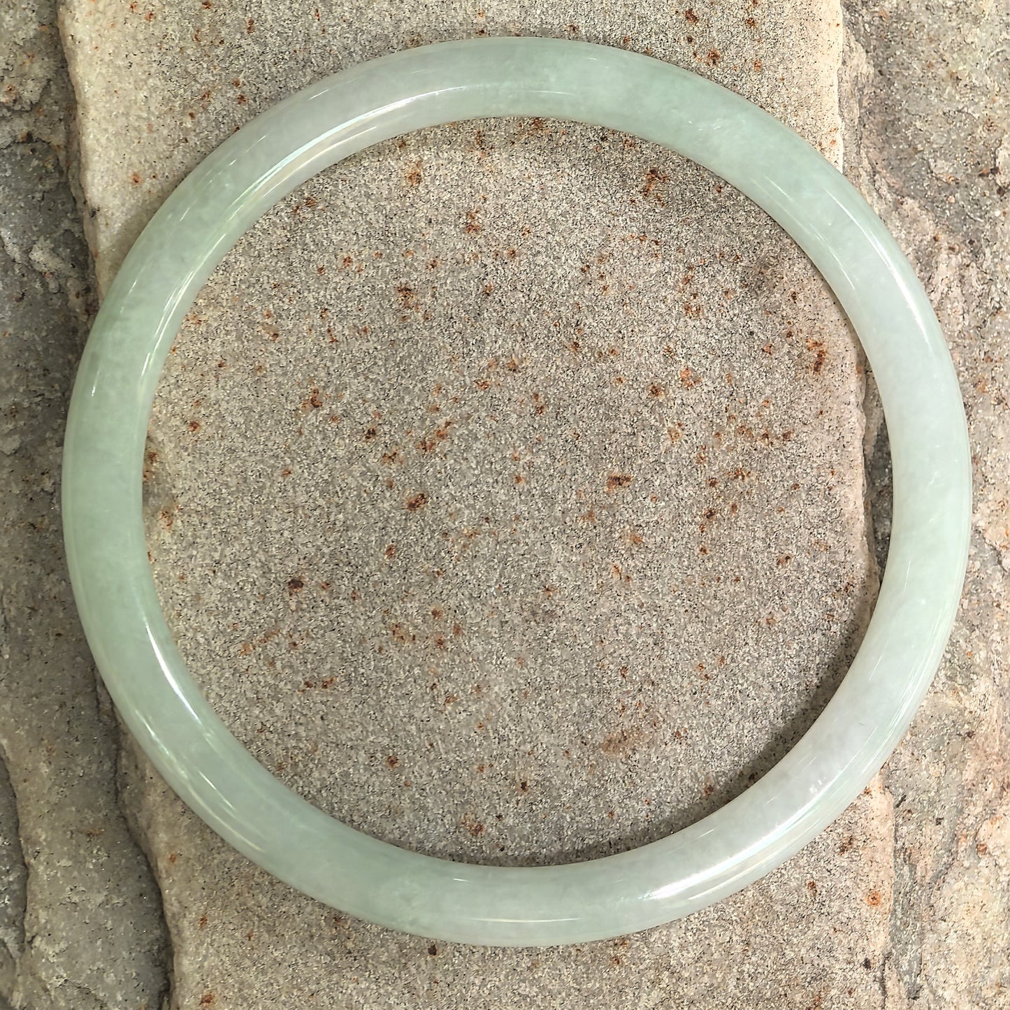 Glutinous jadeite slim round-bar bangle with soft pale green tone and glossy luster.