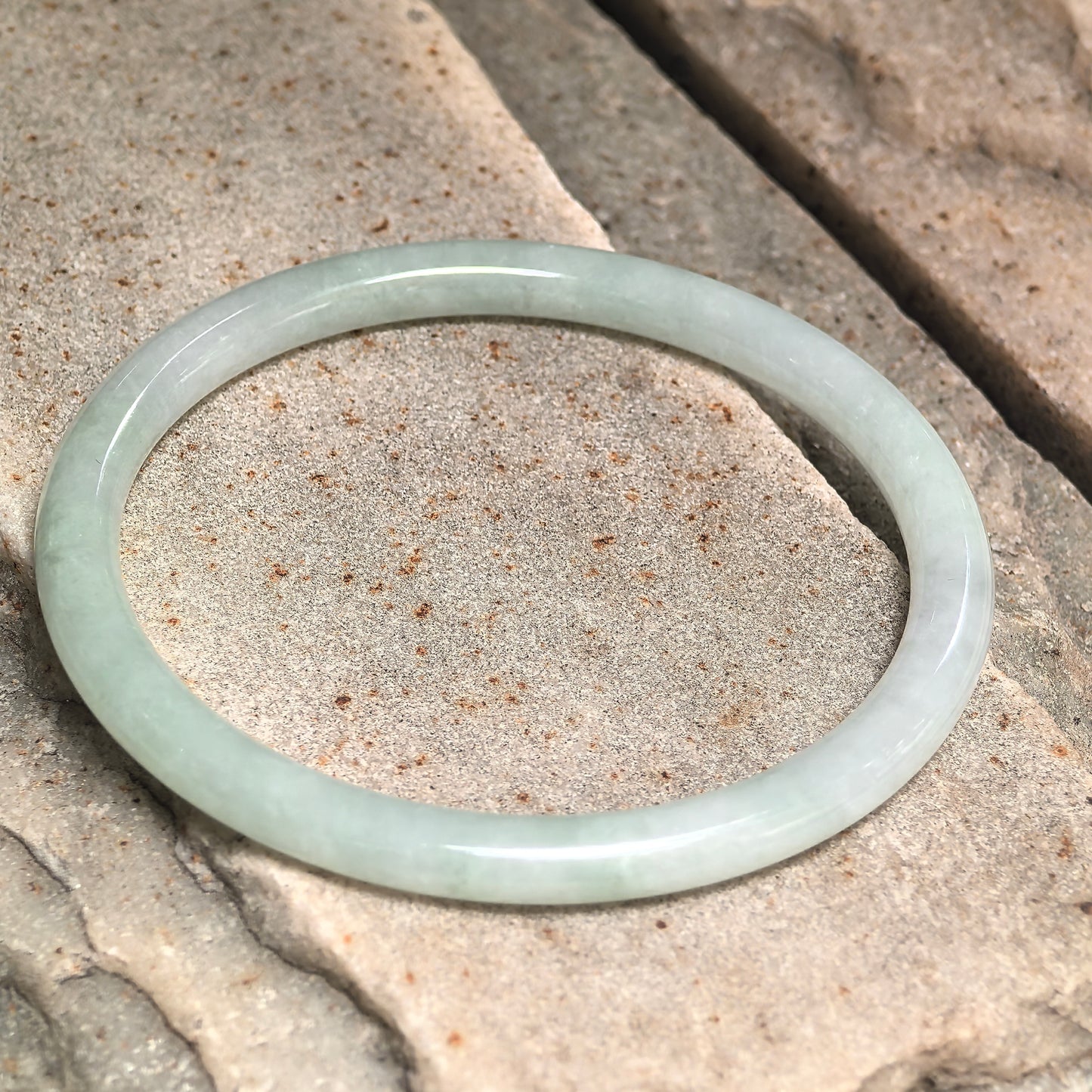 Natural Grade-A light green jadeite bangle displayed on stone background.