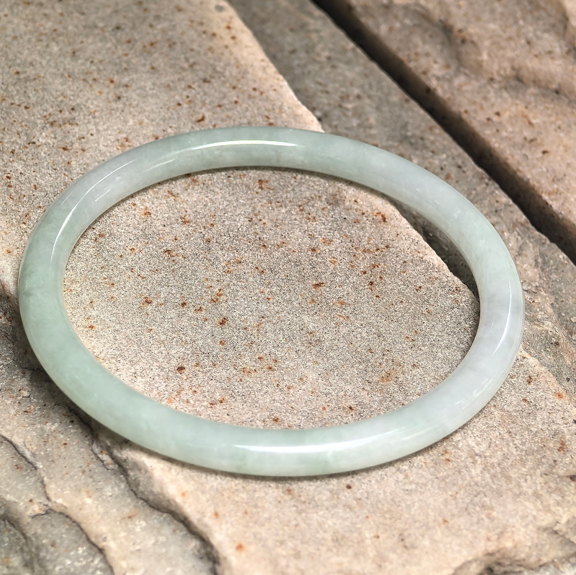 Natural Grade-A light green jadeite bangle displayed on stone background.