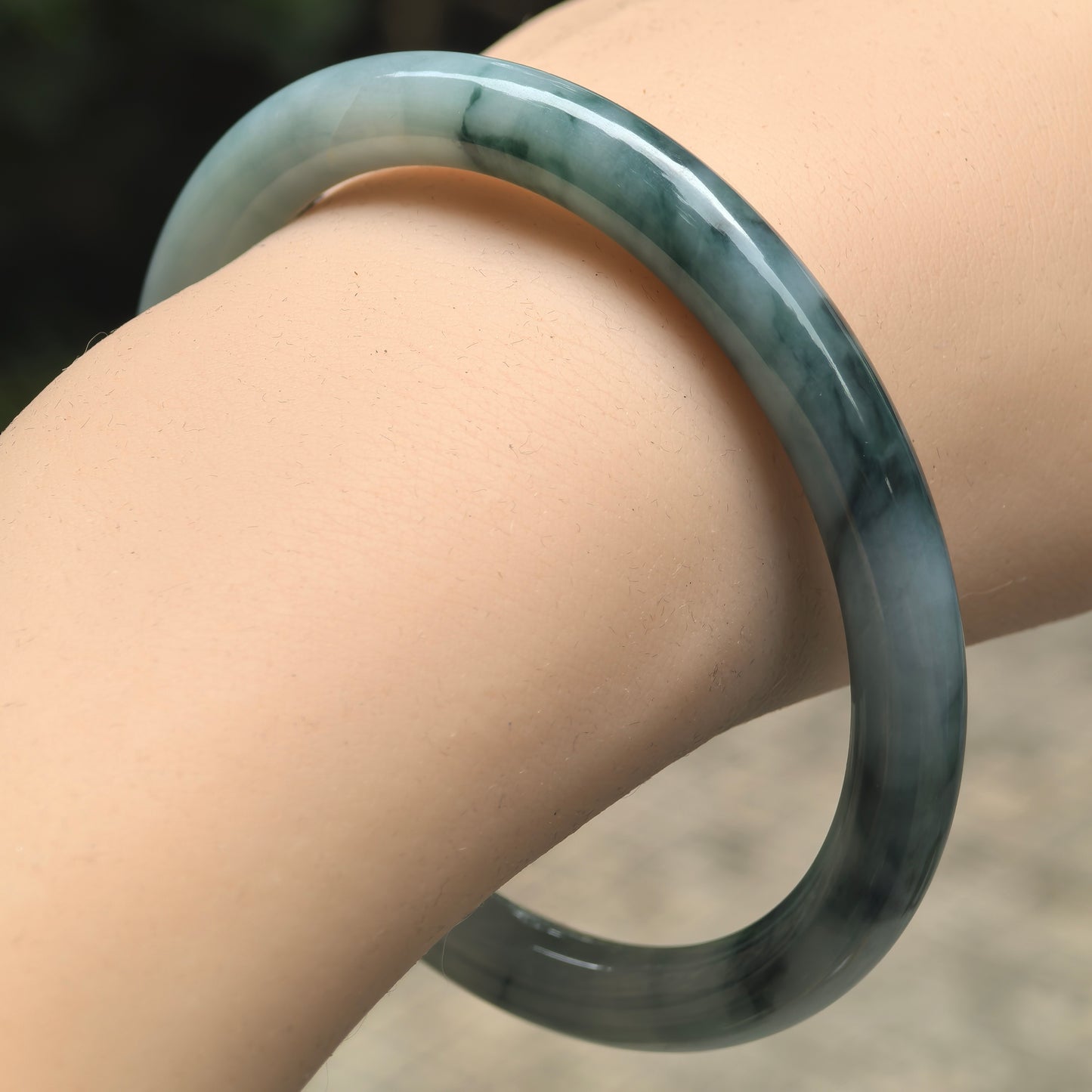 Natural Grade-A glutinous deep green floating flower round-bar jadeite bangle worn on wrist.