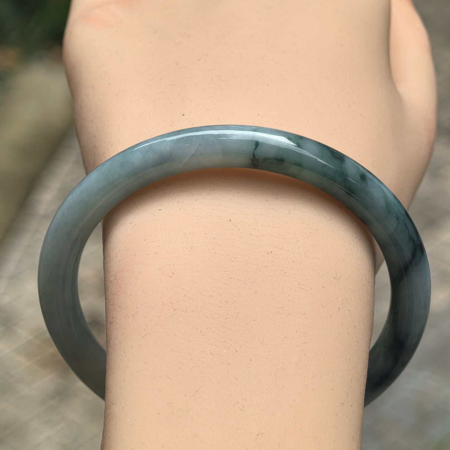 Close-up of deep green floating flower jadeite bangle showing glossy round-bar shape.
