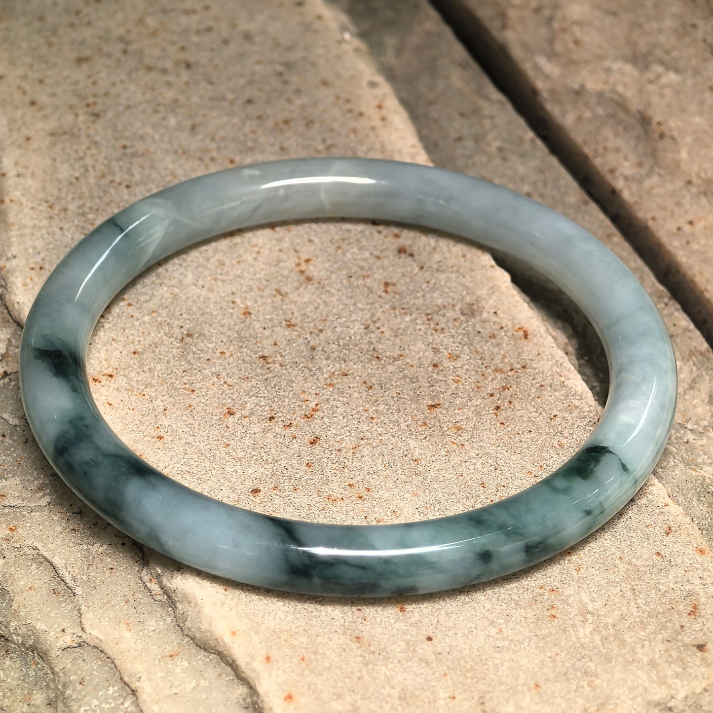 Side view of natural Grade-A jadeite bangle showing rounded profile and deep green color areas.