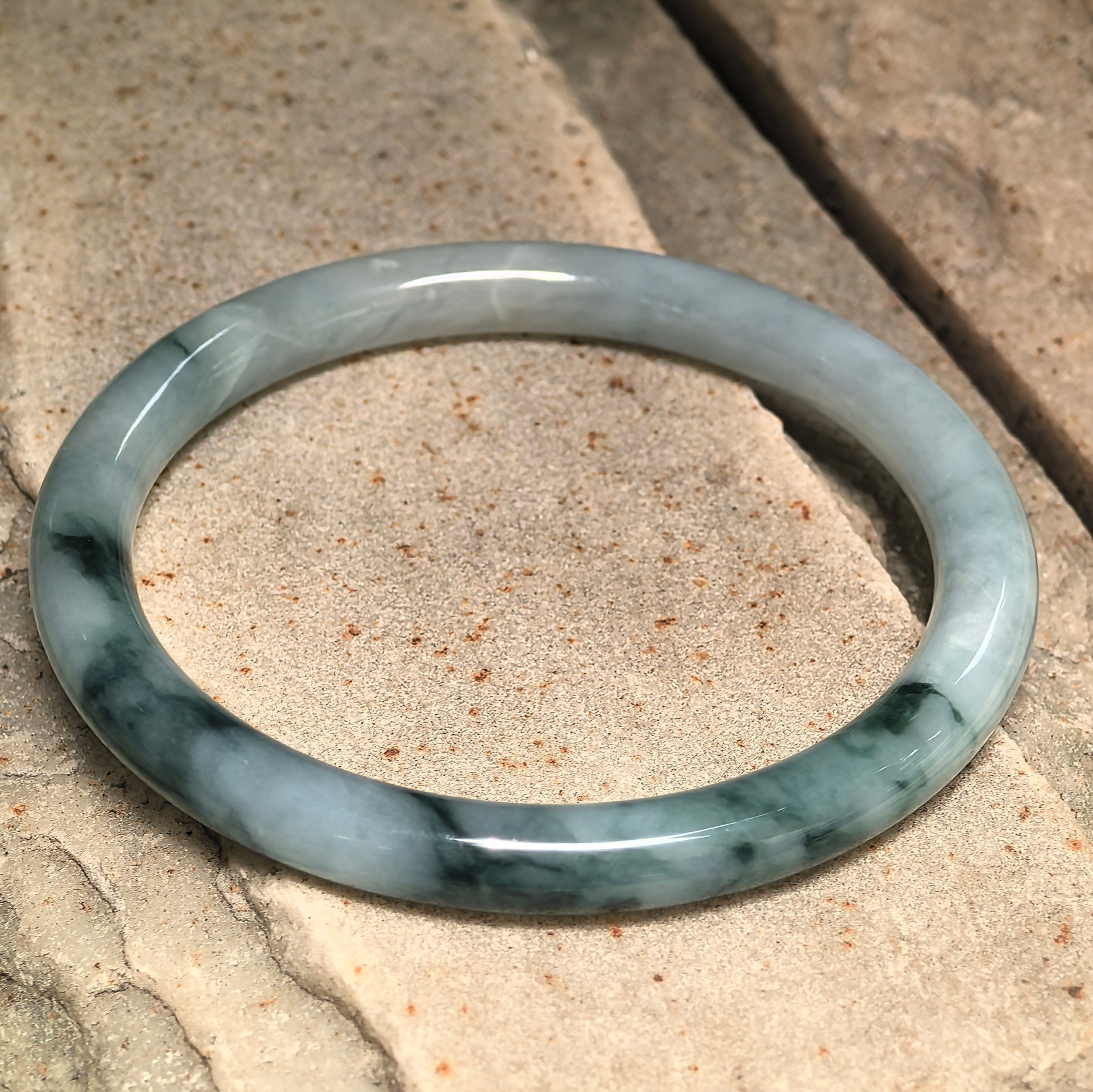 Side view of natural Grade-A jadeite bangle showing rounded profile and deep green color areas.