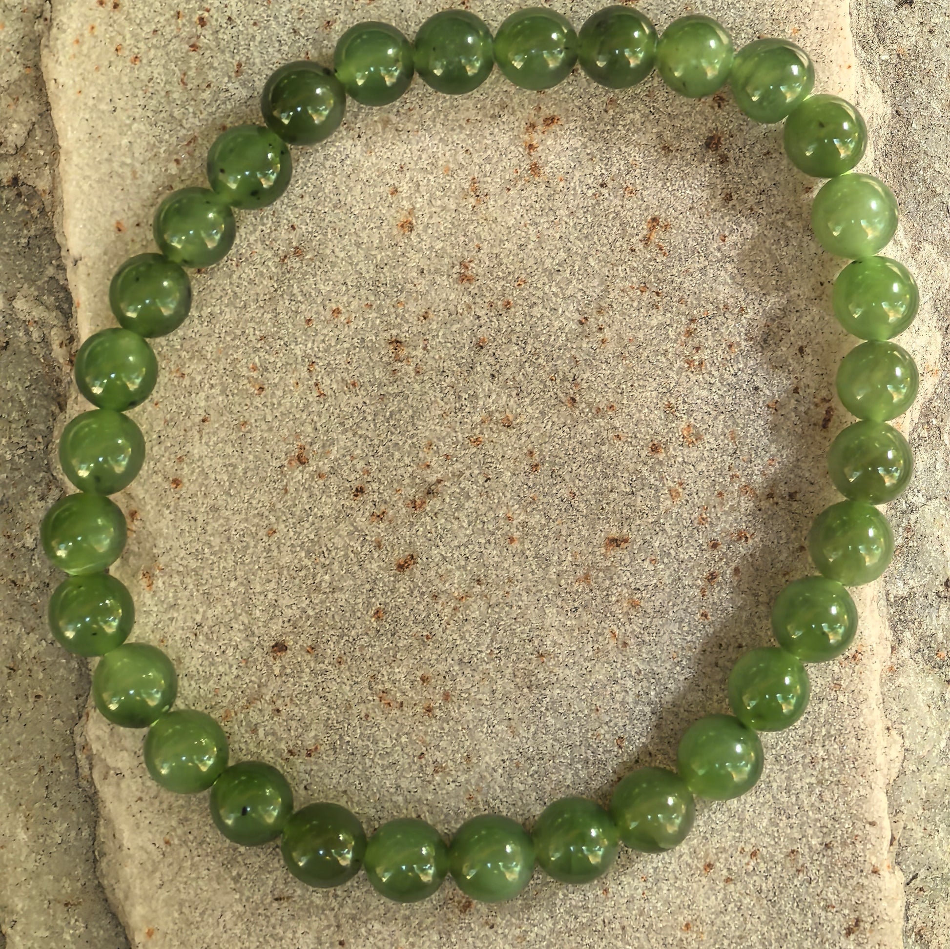 Natural Hetian jade bracelet with 31 round green beads displayed on stone background.