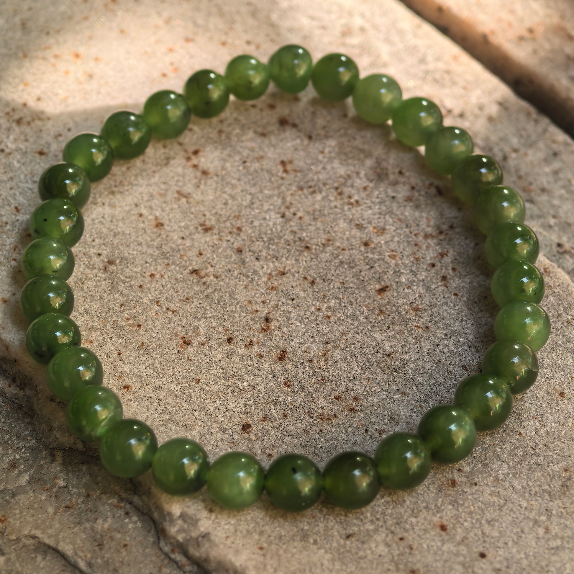 Green nephrite elastic bead bracelet showing natural black spots and black lines.