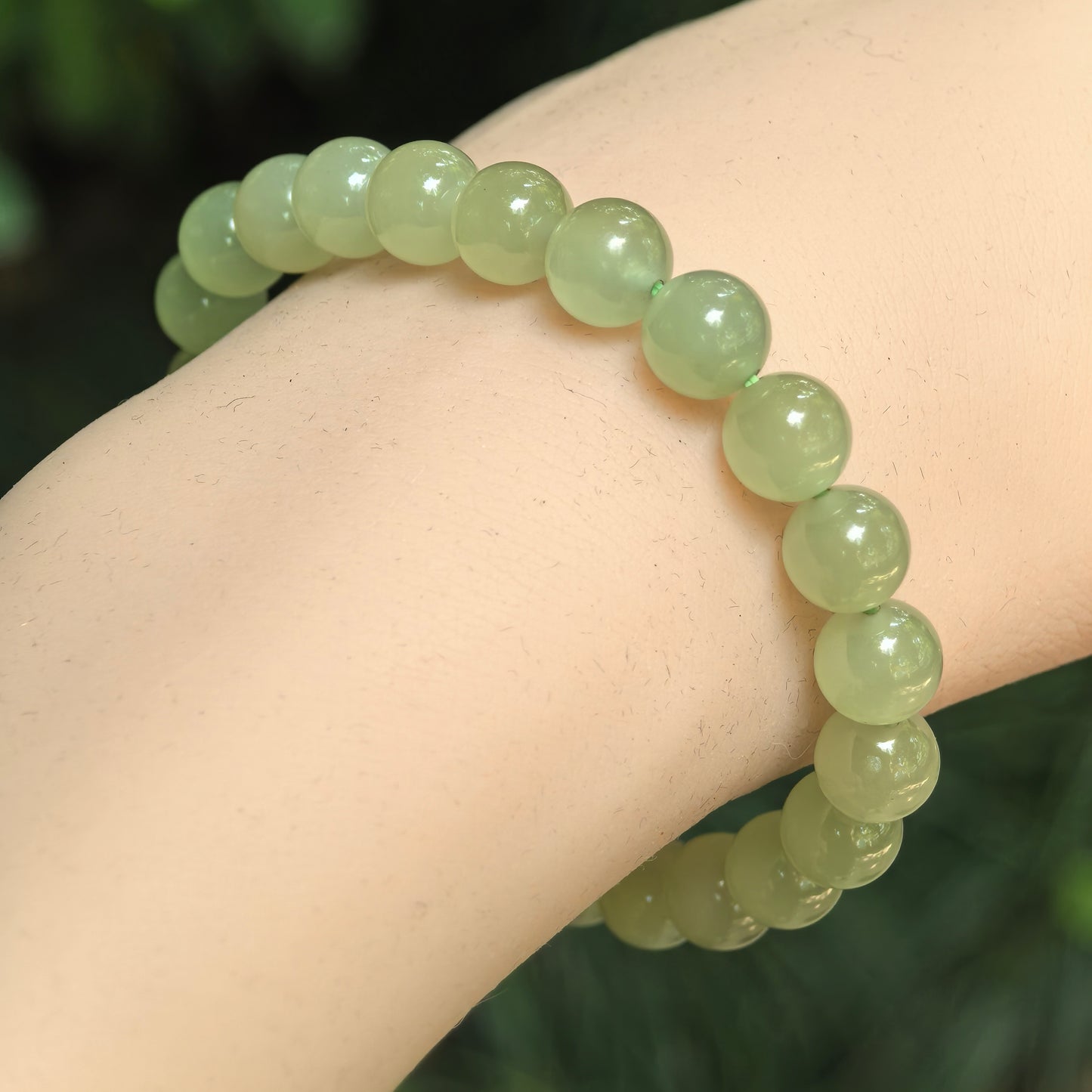 Natural celadon green Hetian jade 8mm bead bracelet worn on wrist.