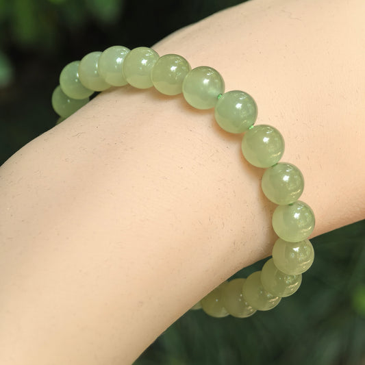 Natural celadon green Hetian jade 8mm bead bracelet worn on wrist.