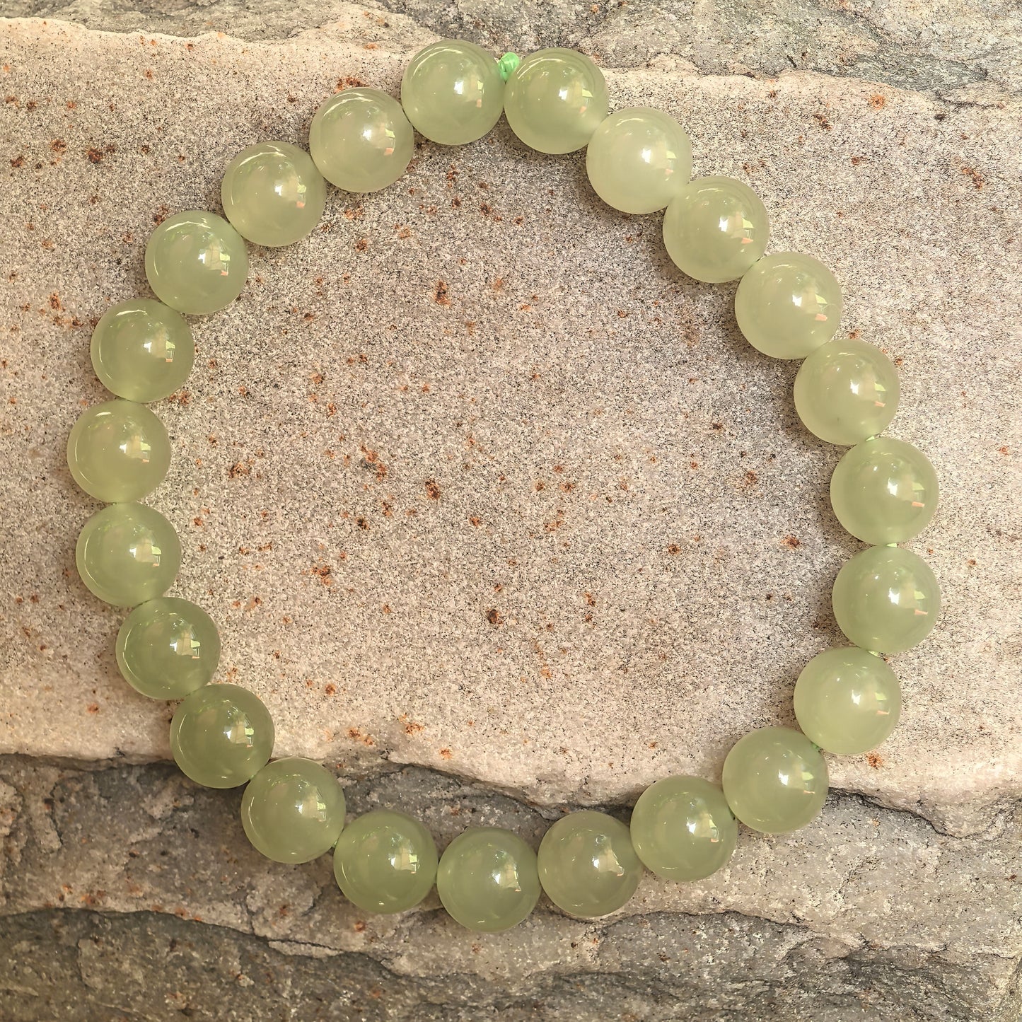 Natural Hetian jade bracelet with 23 round green beads displayed on stone background.