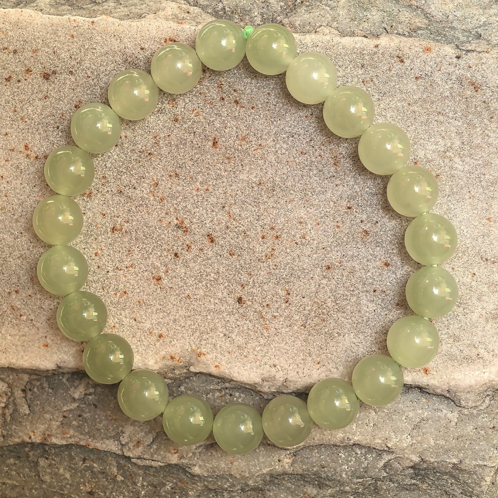 Natural Hetian jade bracelet with 23 round green beads displayed on stone background.
