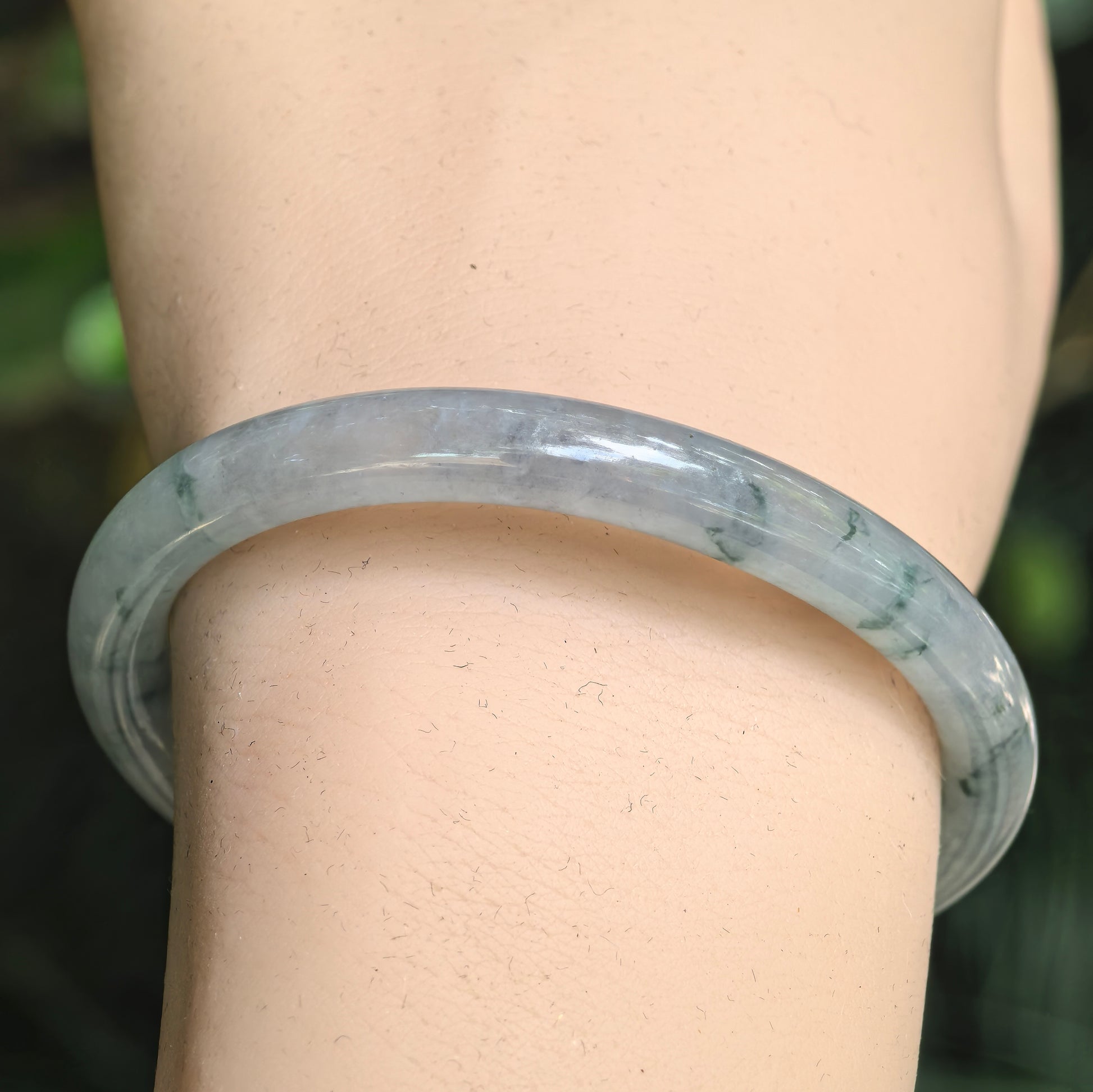 Close-up of a light green jadeite oval bangle with deep green floating flower patterns.