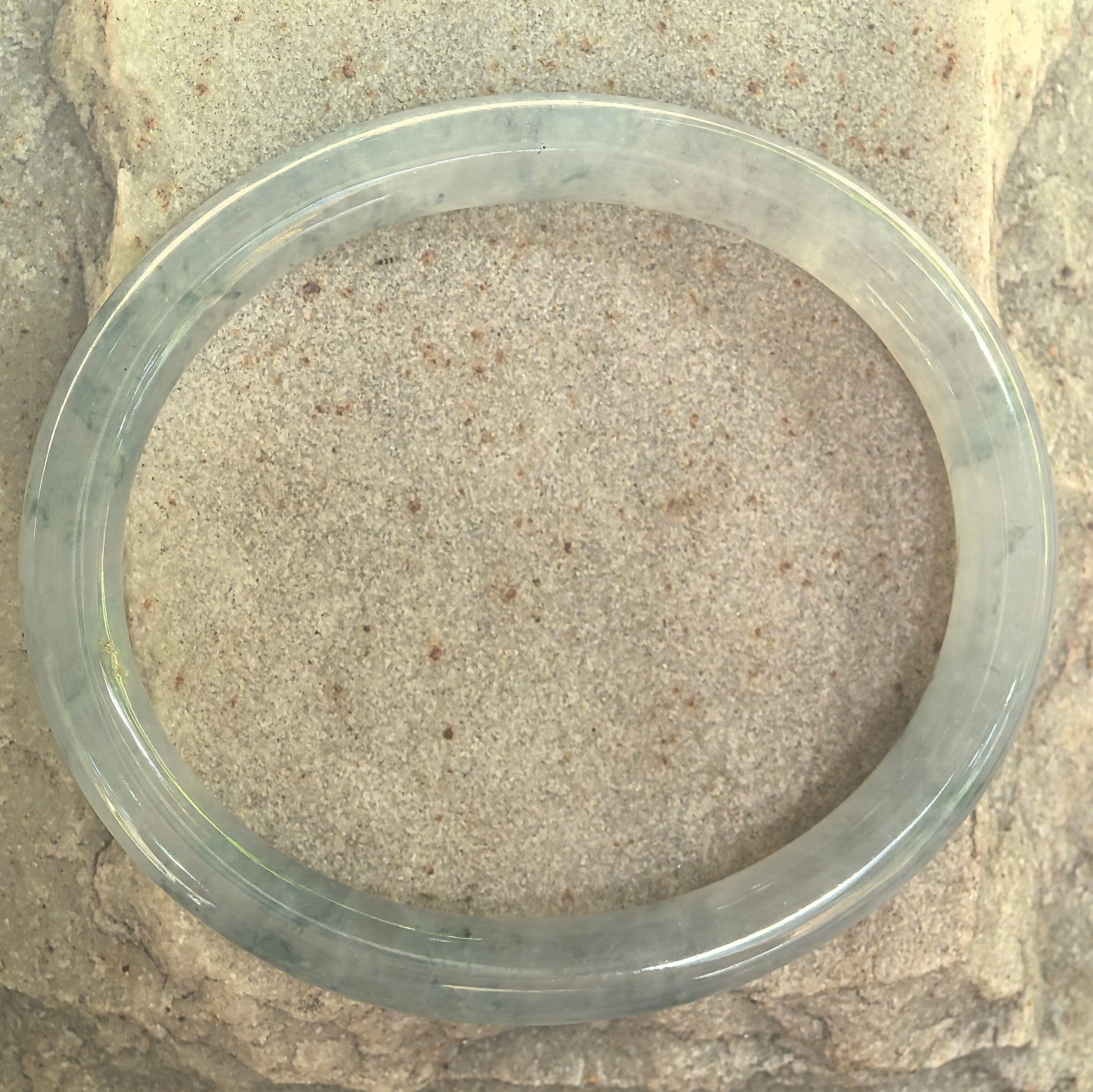 Top view of a slim oval jadeite bangle showing translucent green texture.
