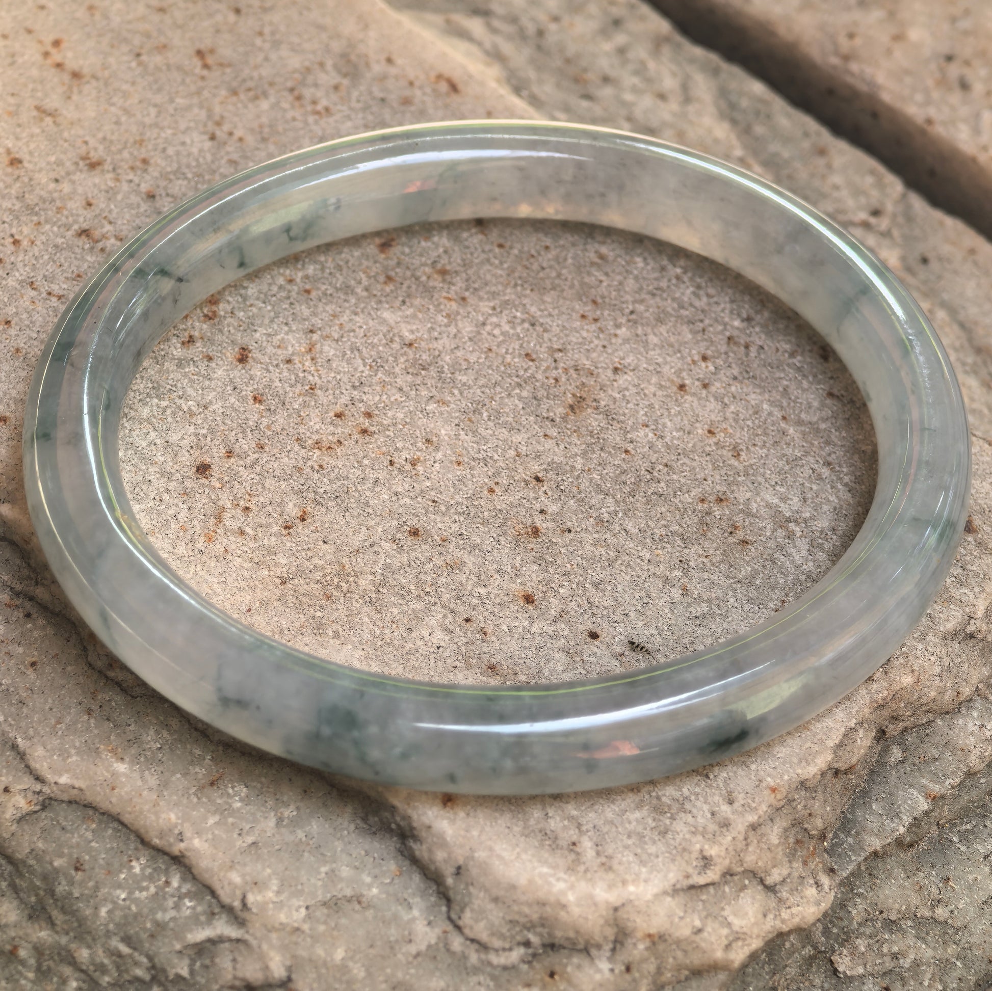 Angled view of a natural jadeite bangle with floating flower patterns and polished surface.
