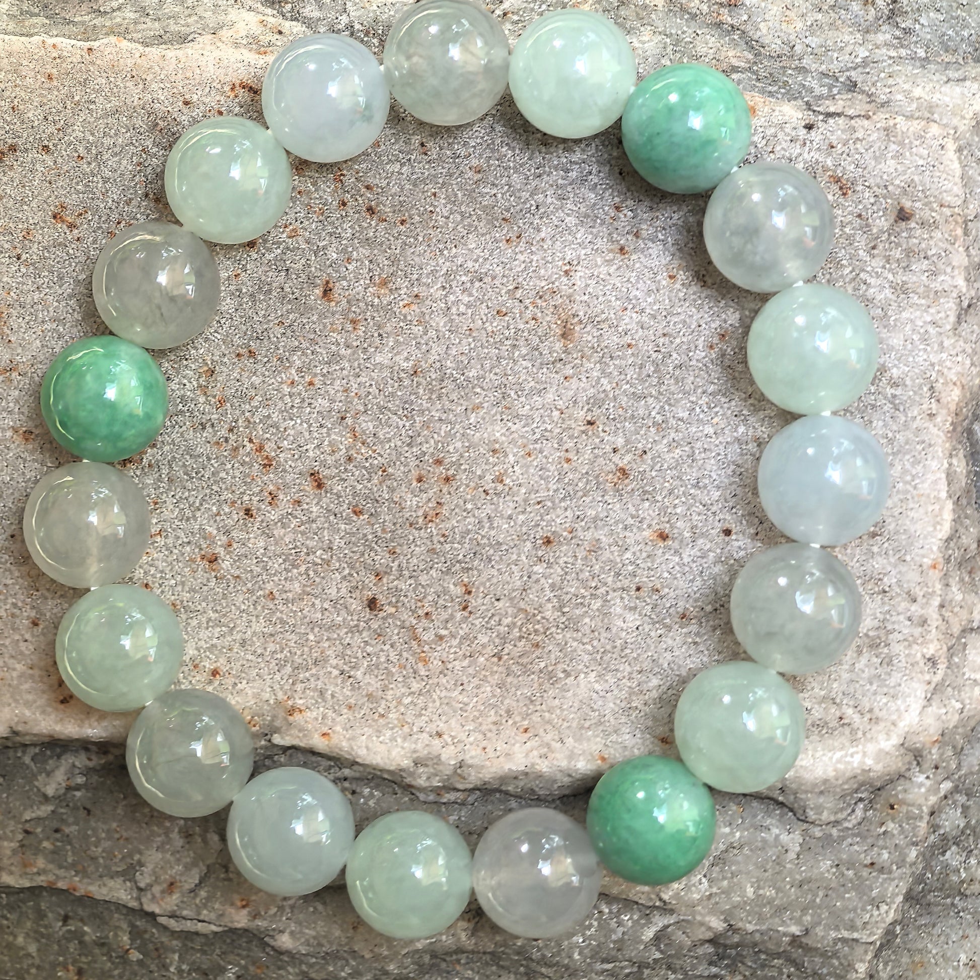 Natural jadeite bracelet with 18 round beads displayed on stone background.
