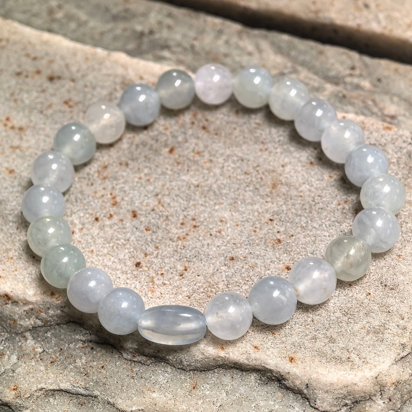 White glutinous-icy jadeite bead bracelet displayed on stone background.
