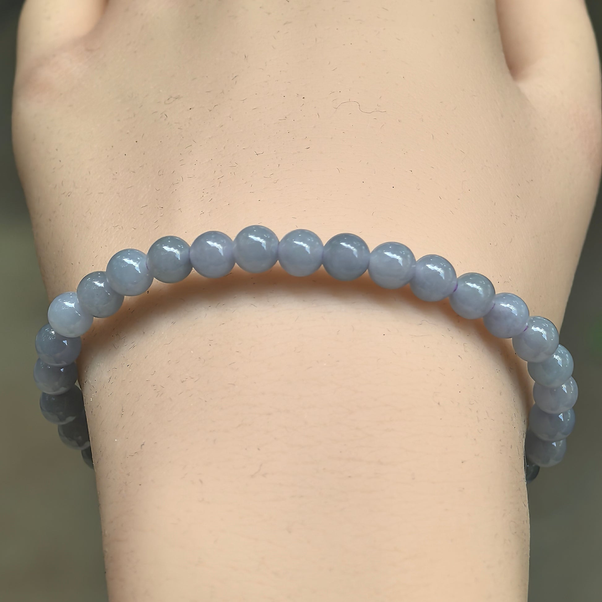 Close-up of blue-purple jadeite round bead bracelet with glossy polished surface.