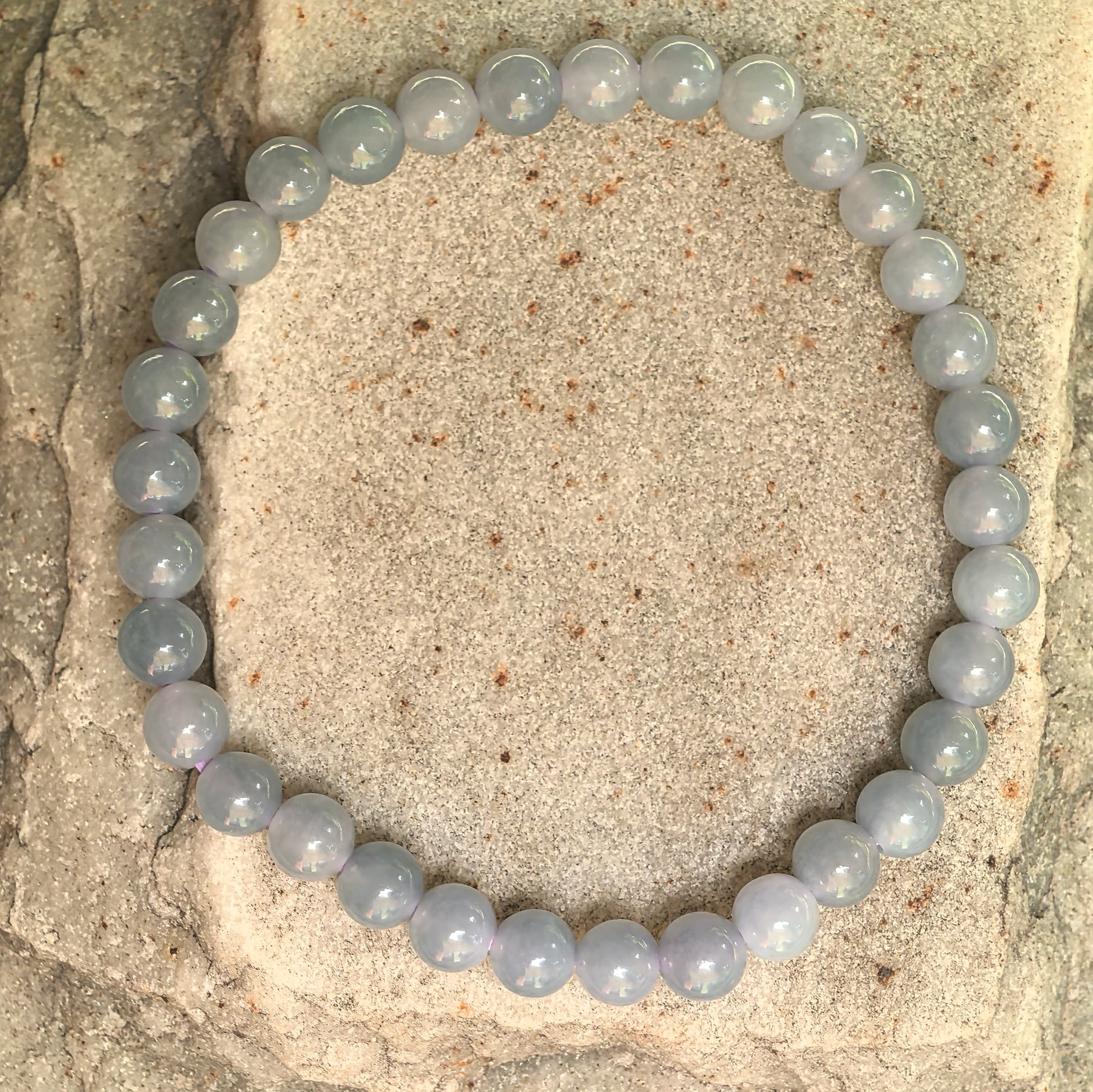 Natural jadeite bracelet with small 5.5mm blue-purple beads displayed on stone background.