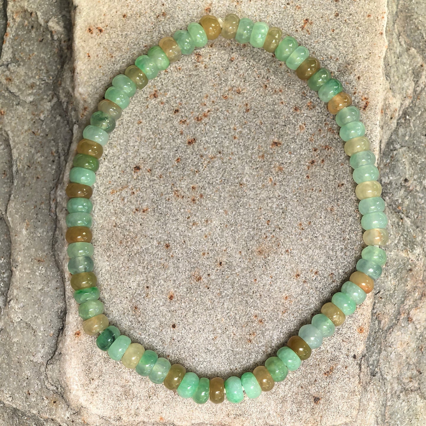 Natural jadeite bracelet with small abacus-shaped beads displayed on stone background.