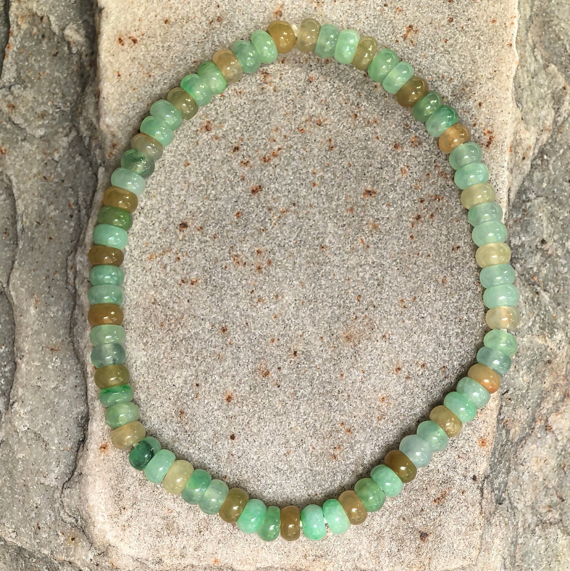 Natural jadeite bracelet with small abacus-shaped beads displayed on stone background.
