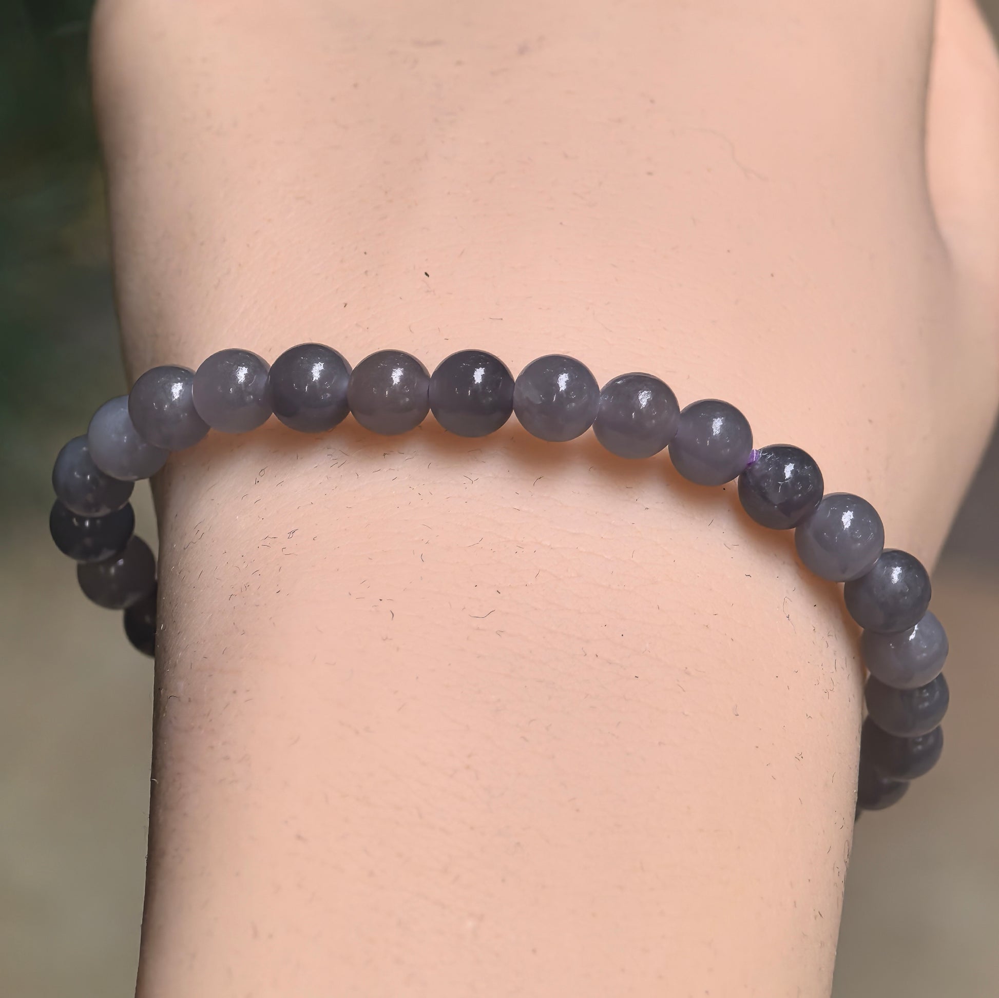 Close-up of gray-purple Hetian jade round bead bracelet under natural light.