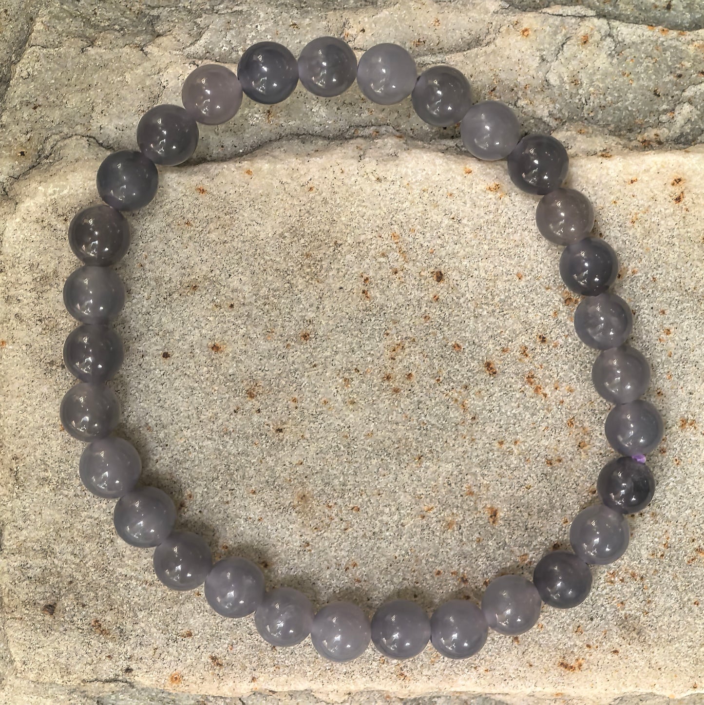 Smoky purple Hetian jade bracelet displayed on stone background.