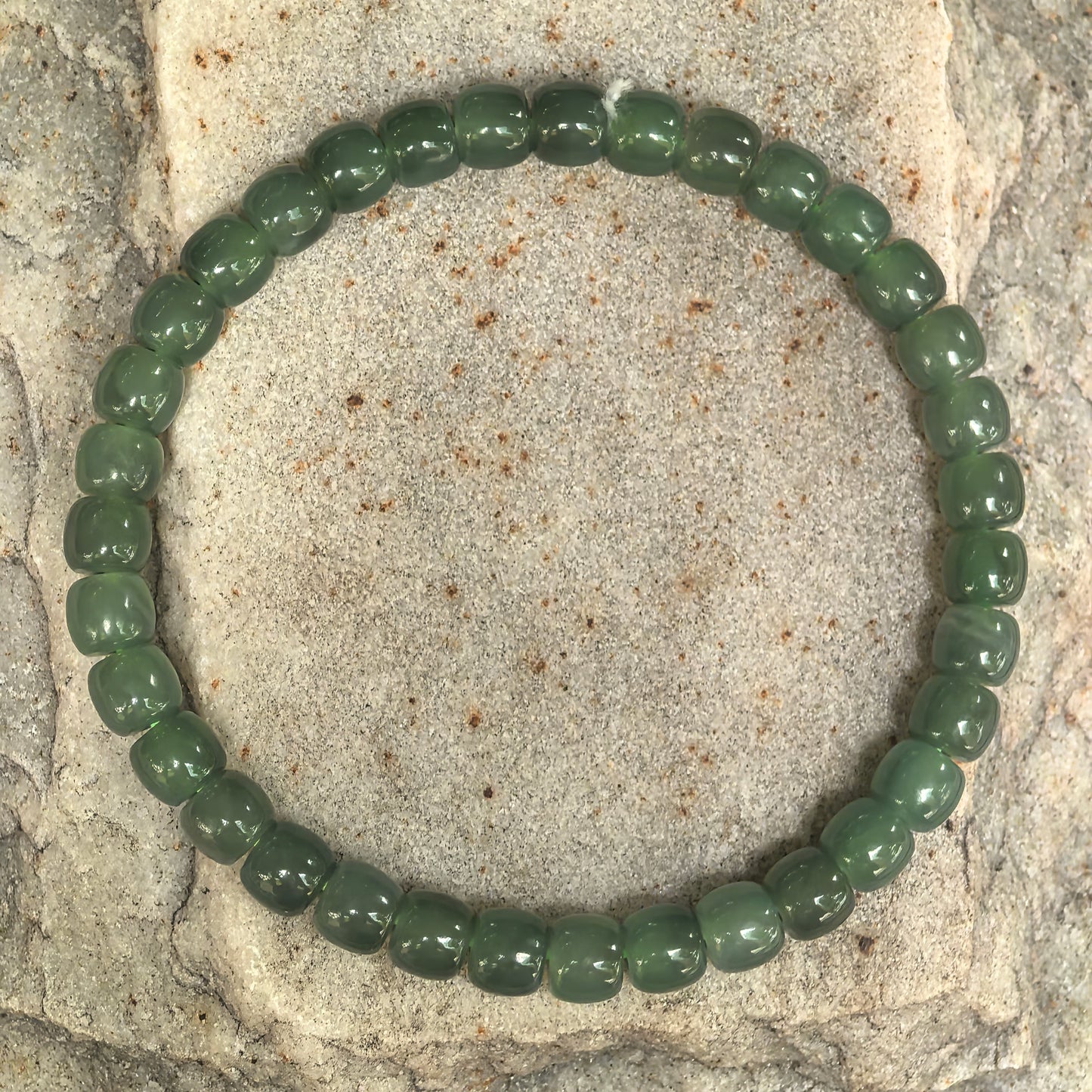 Natural Hetian jade bracelet with 35 abacus-shaped green beads displayed on stone background.