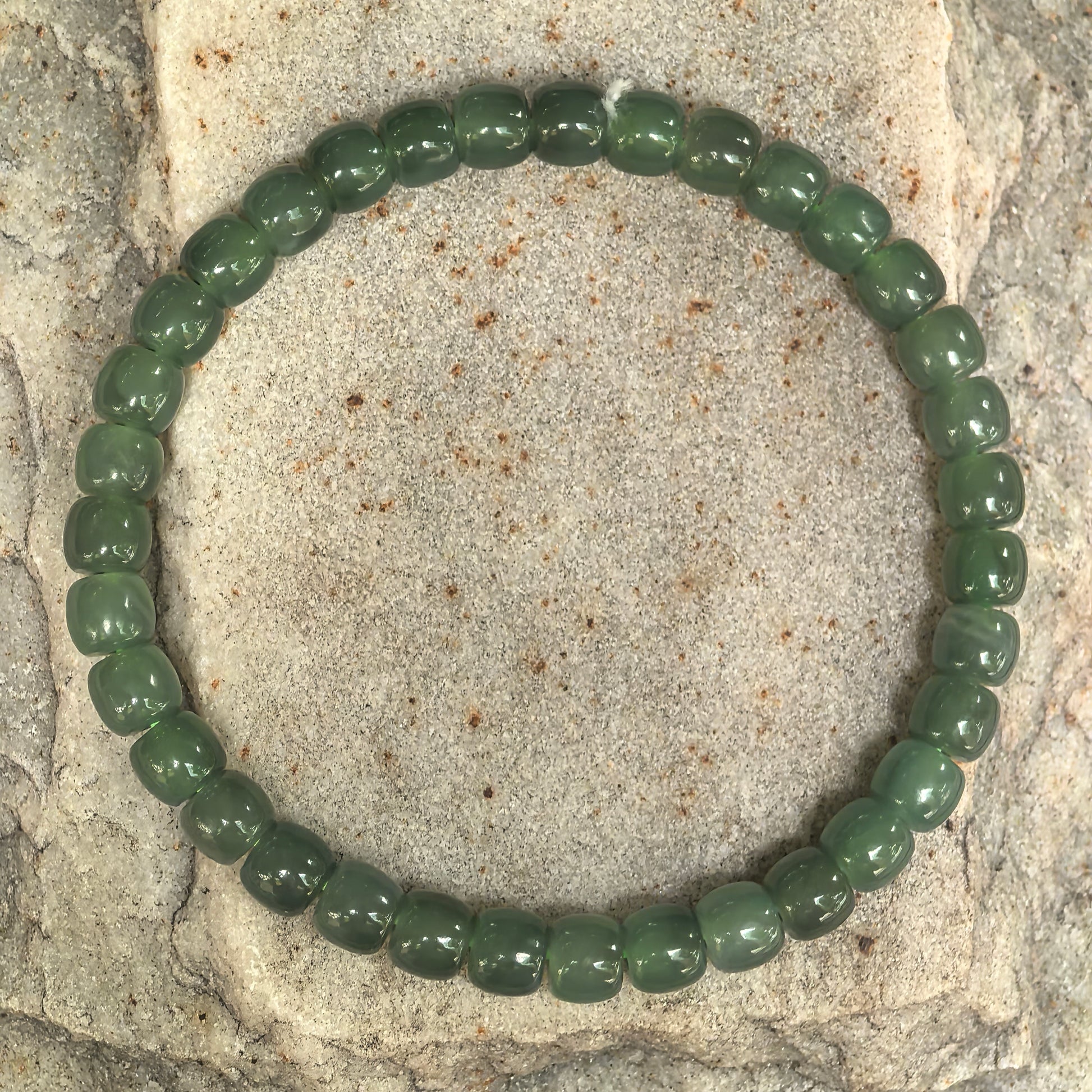 Natural Hetian jade bracelet with 35 abacus-shaped green beads displayed on stone background.