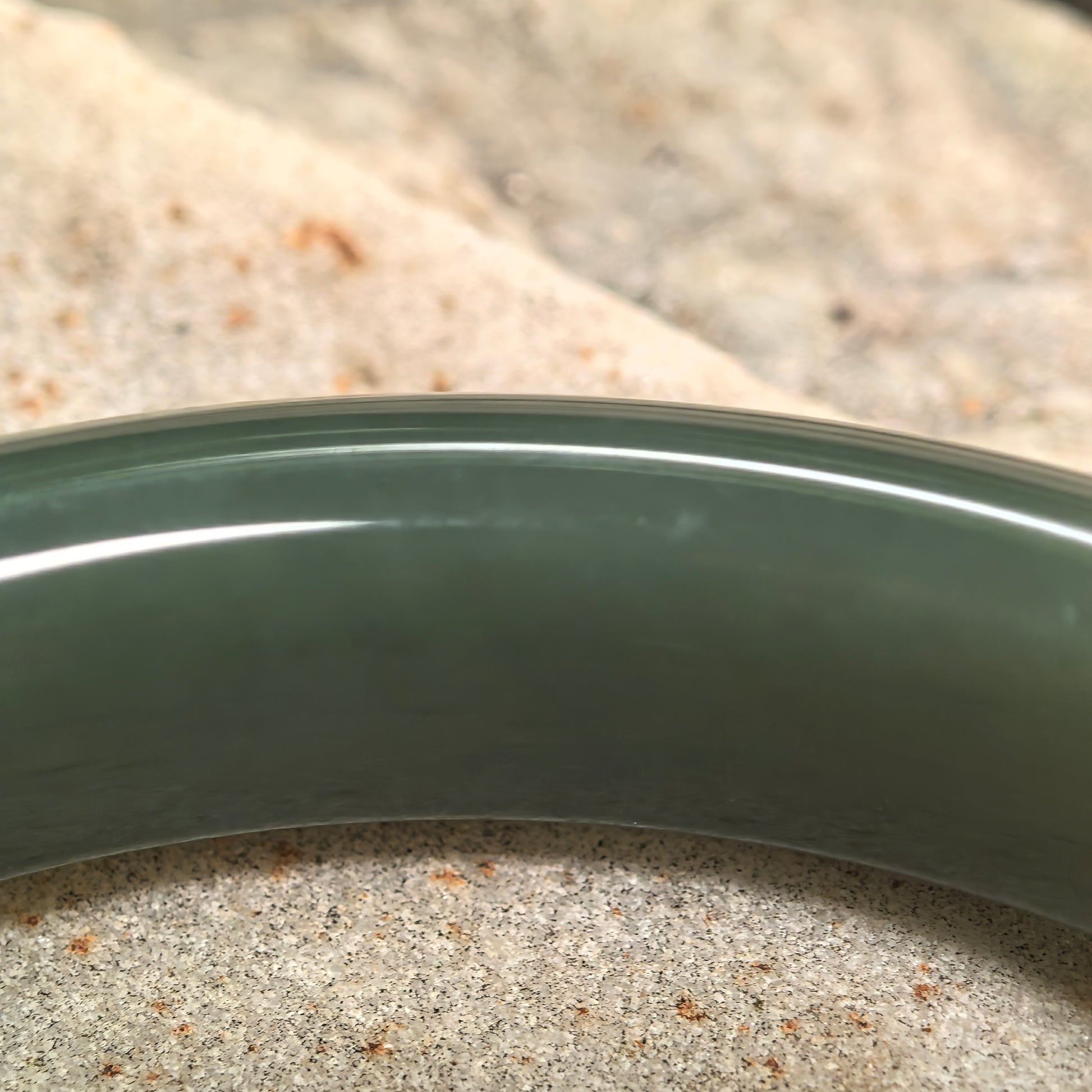 Natural Hetian jade bangle displayed on stone background with deep green color and classic D-shape profile.