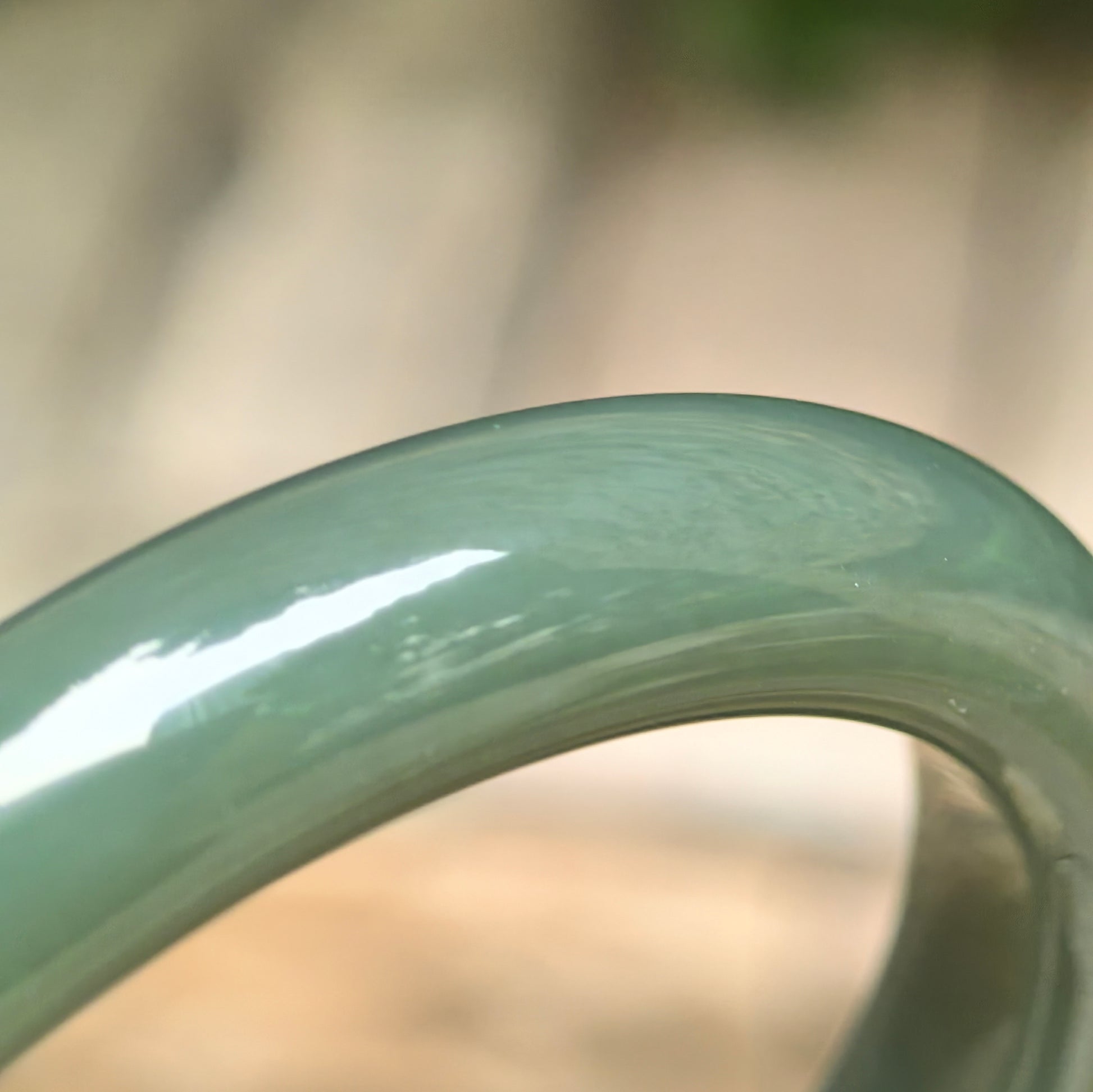 Close-up of dark green Hetian jade bracelet showing smooth glossy surface and understated color tone.