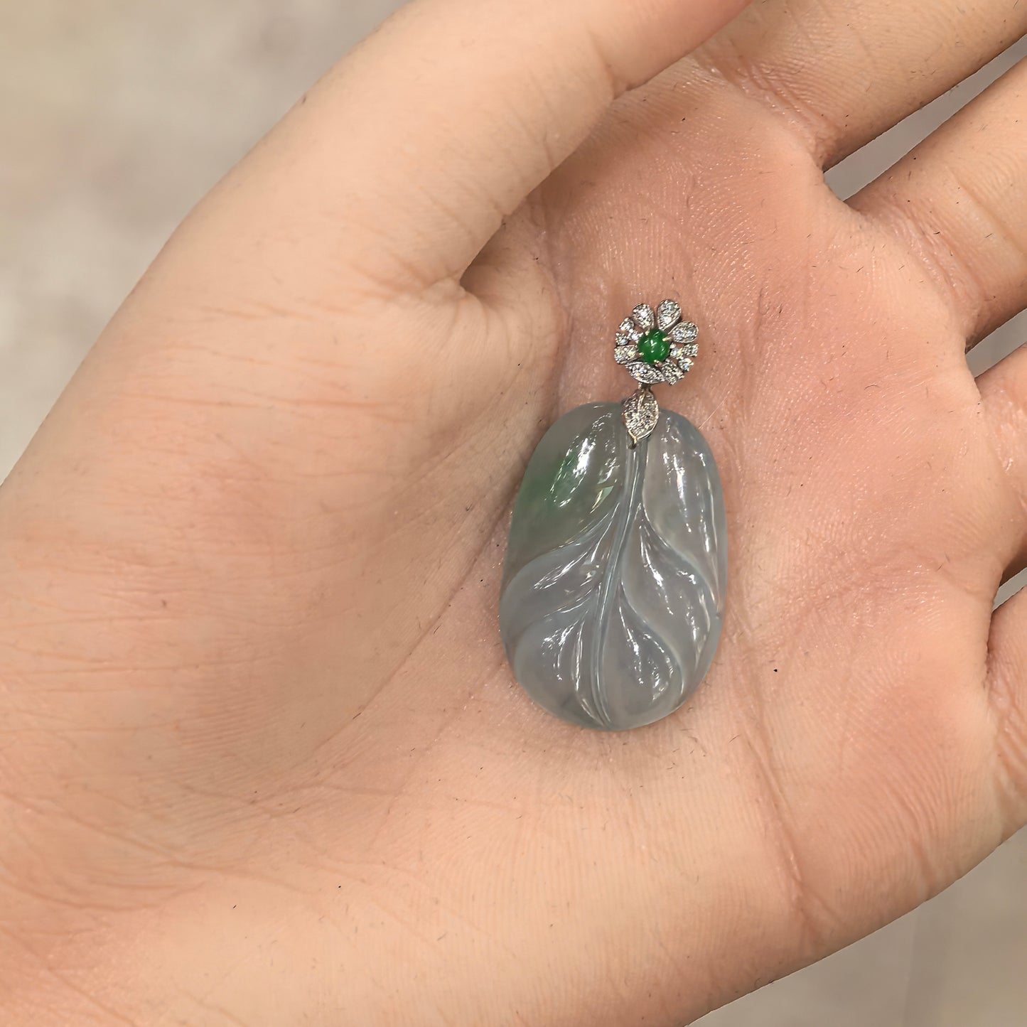 Handheld view of jadeite pendant showing size scale, polished surface, and natural internal jadeite structure under light.
