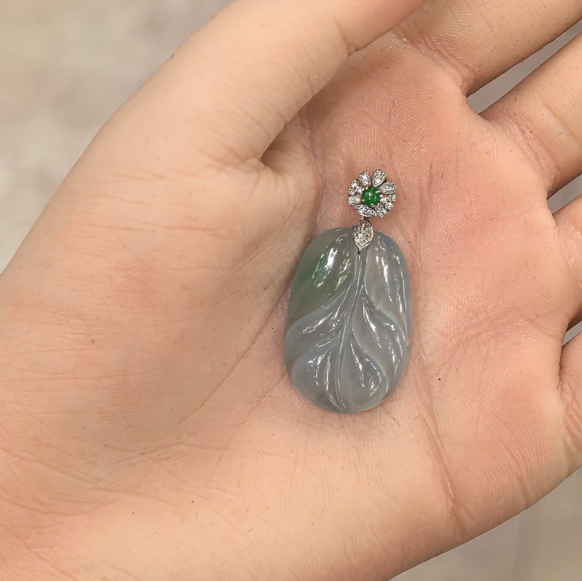 Handheld view of jadeite pendant showing size scale, polished surface, and natural internal jadeite structure under light.