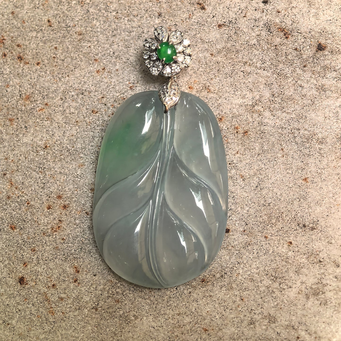 Close-up of Burmese jadeite leaf pendant highlighting icy translucency, natural green tone, and diamond-set gold mounting structure.