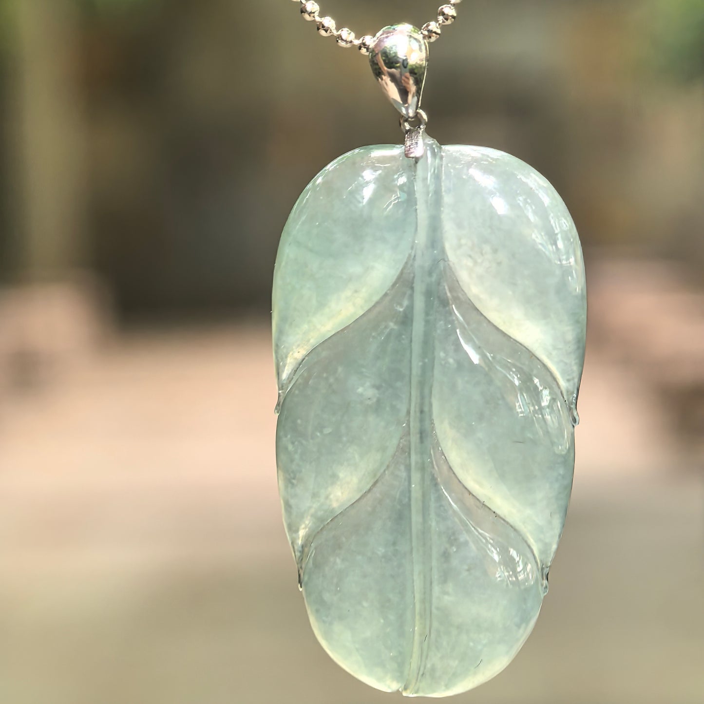 Natural icy glutinous light green jadeite leaf pendant with carved leaf structure and 18K gold diamond-set mounting showing translucent texture under light.