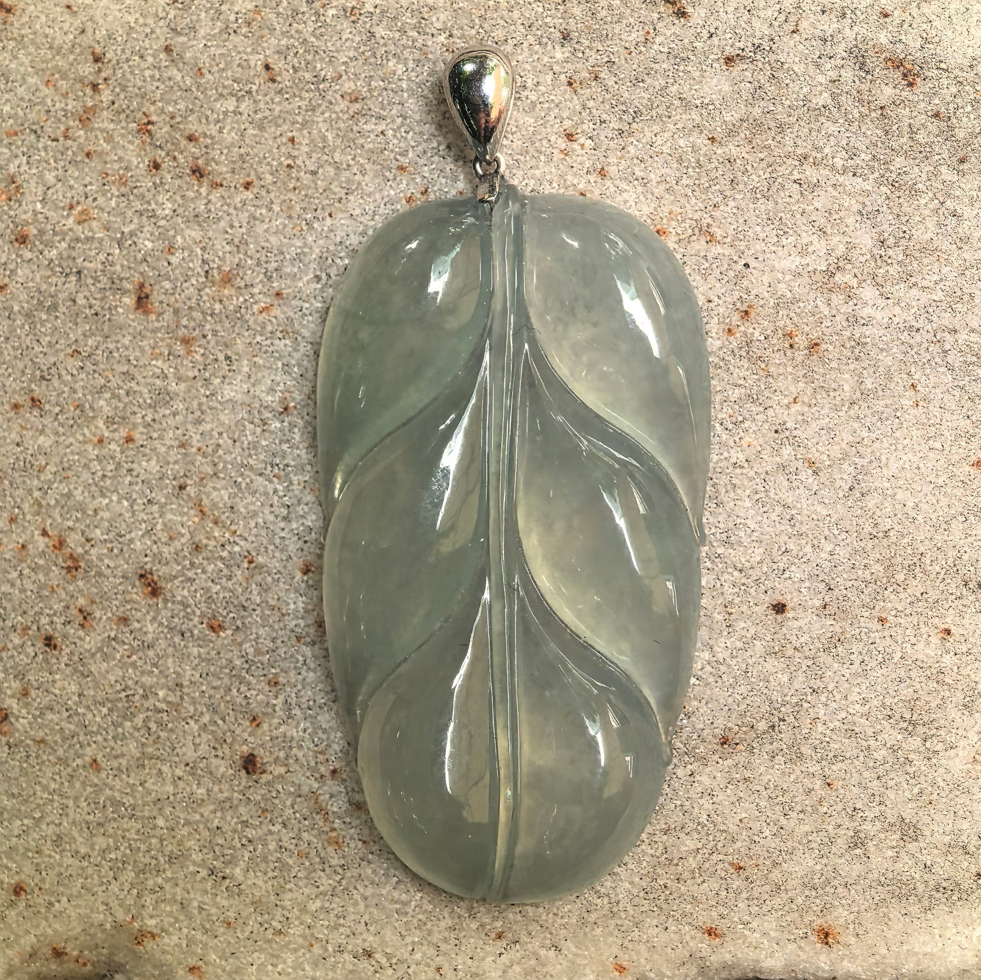 Close-up of Burmese jadeite pendant highlighting icy glutinous texture, soft green tone, and polished surface finish.