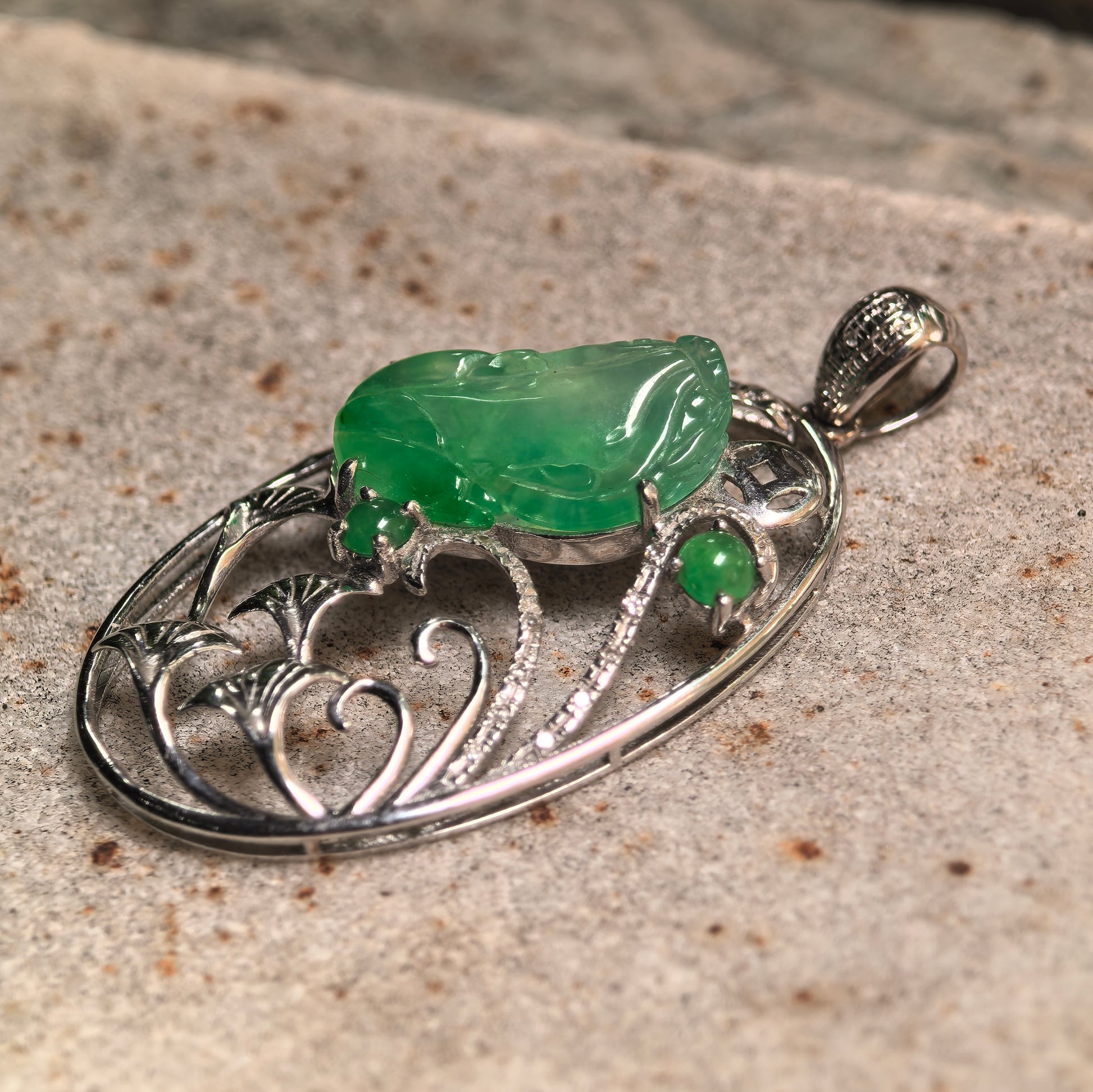 Jade pendant placed on stone surface showing natural Burmese jade texture and 18K gold craftsmanship detail.
