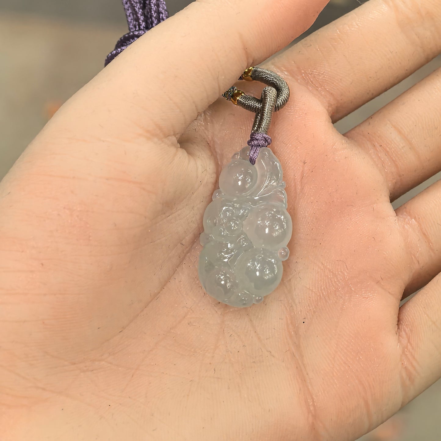Pale green jadeite monkey pendant shown in hand with rounded longevity peach carving.