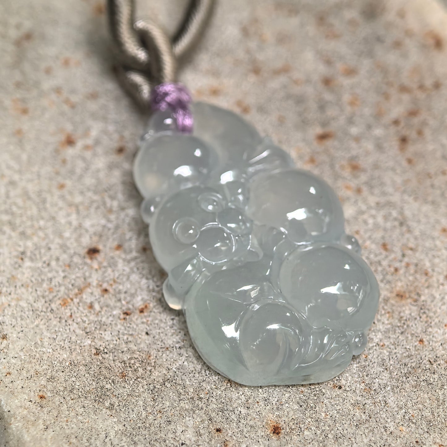 Side view of small pale green jadeite pendant showing carved peach details and compact thickness.