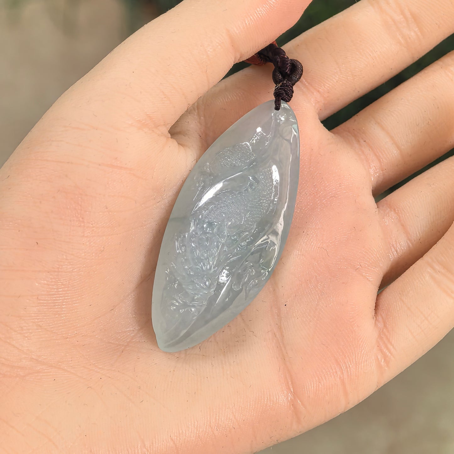 Natural Grade-A light green dragon jadeite pendant shown in hand with cord and smooth rounded outline.