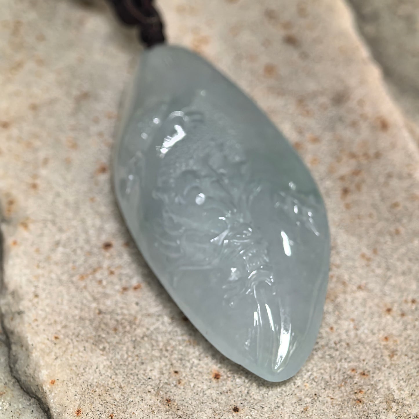 Elongated carved jadeite dragon pendant displayed on stone background with polished glossy finish.