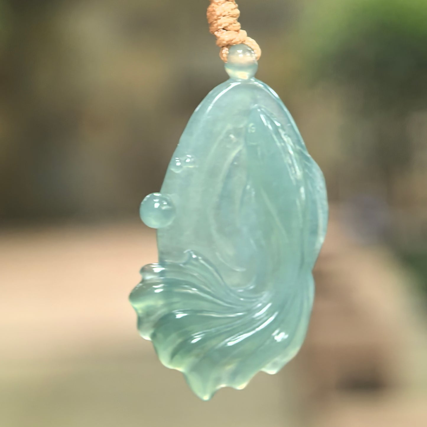 Natural Grade-A icy glutinous deep green fish jadeite pendant hanging on cord with flowing tail carving.