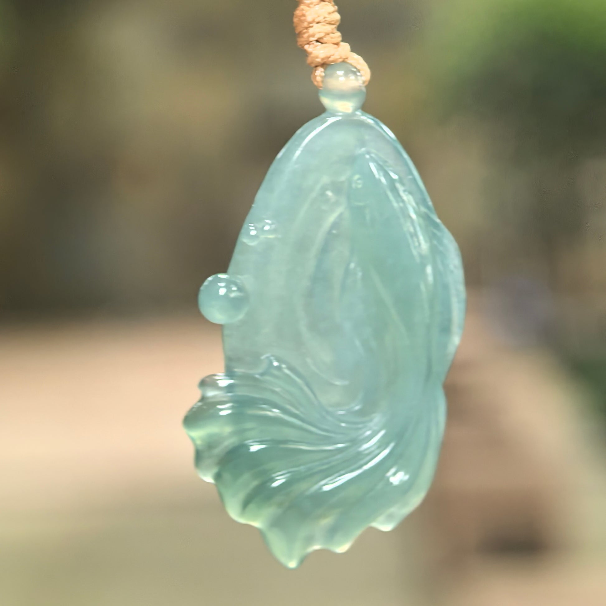 Natural Grade-A icy glutinous deep green fish jadeite pendant hanging on cord with flowing tail carving.