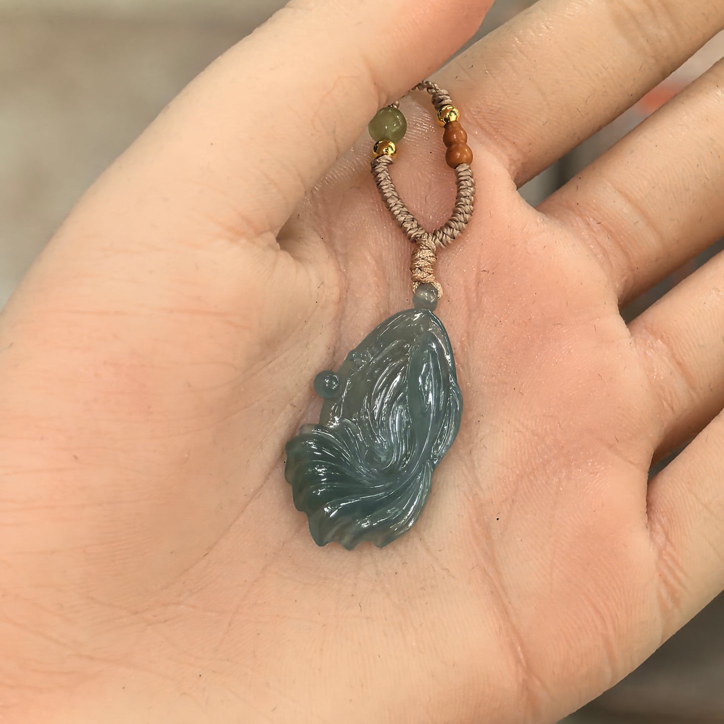 Deep green fish jadeite pendant displayed in hand, showing compact size, watery carving lines, and smooth polished luster.