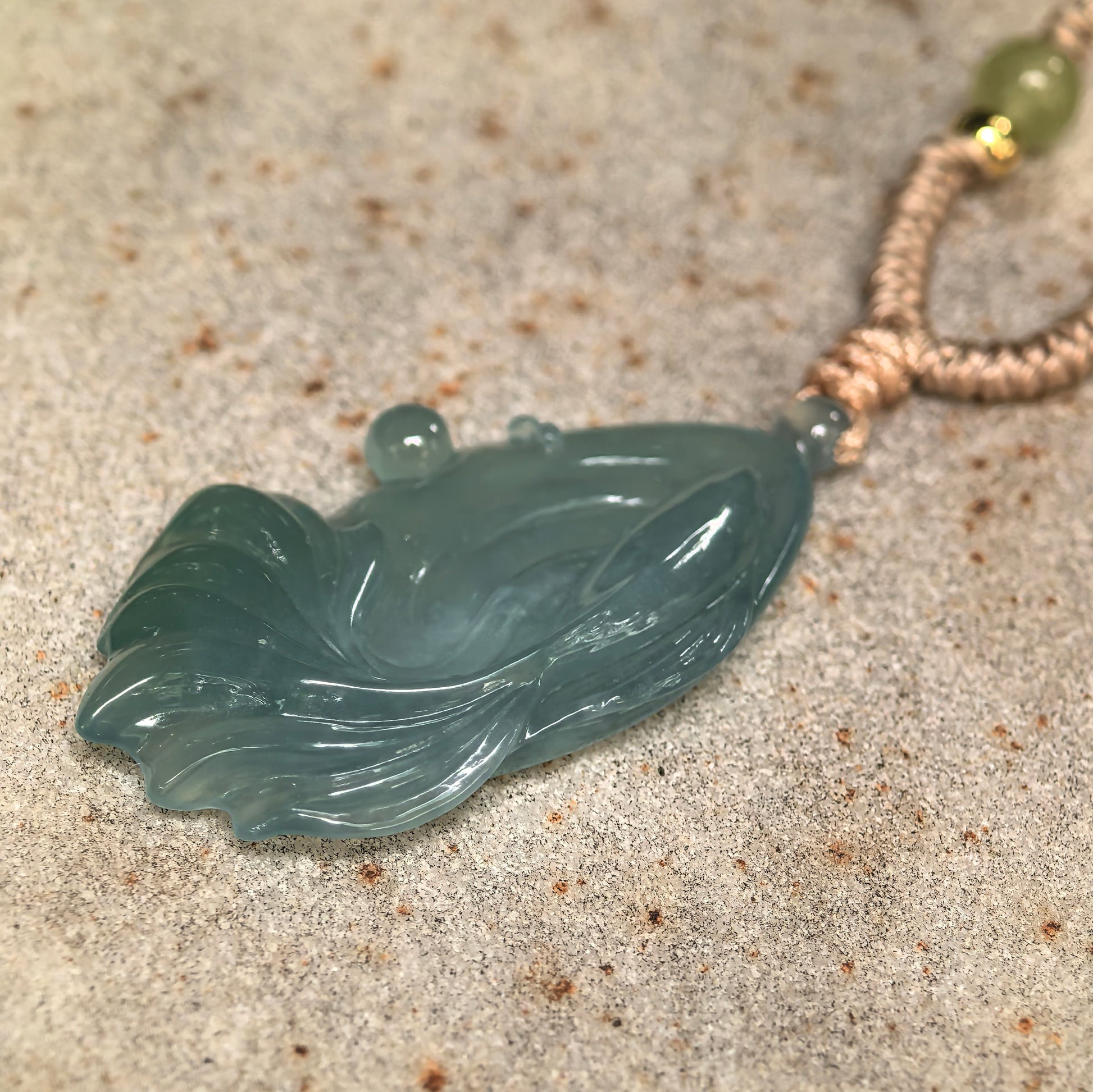 Angled view of deep green fish jadeite pendant showing curved body, carved tail, and translucent blue-green tone.