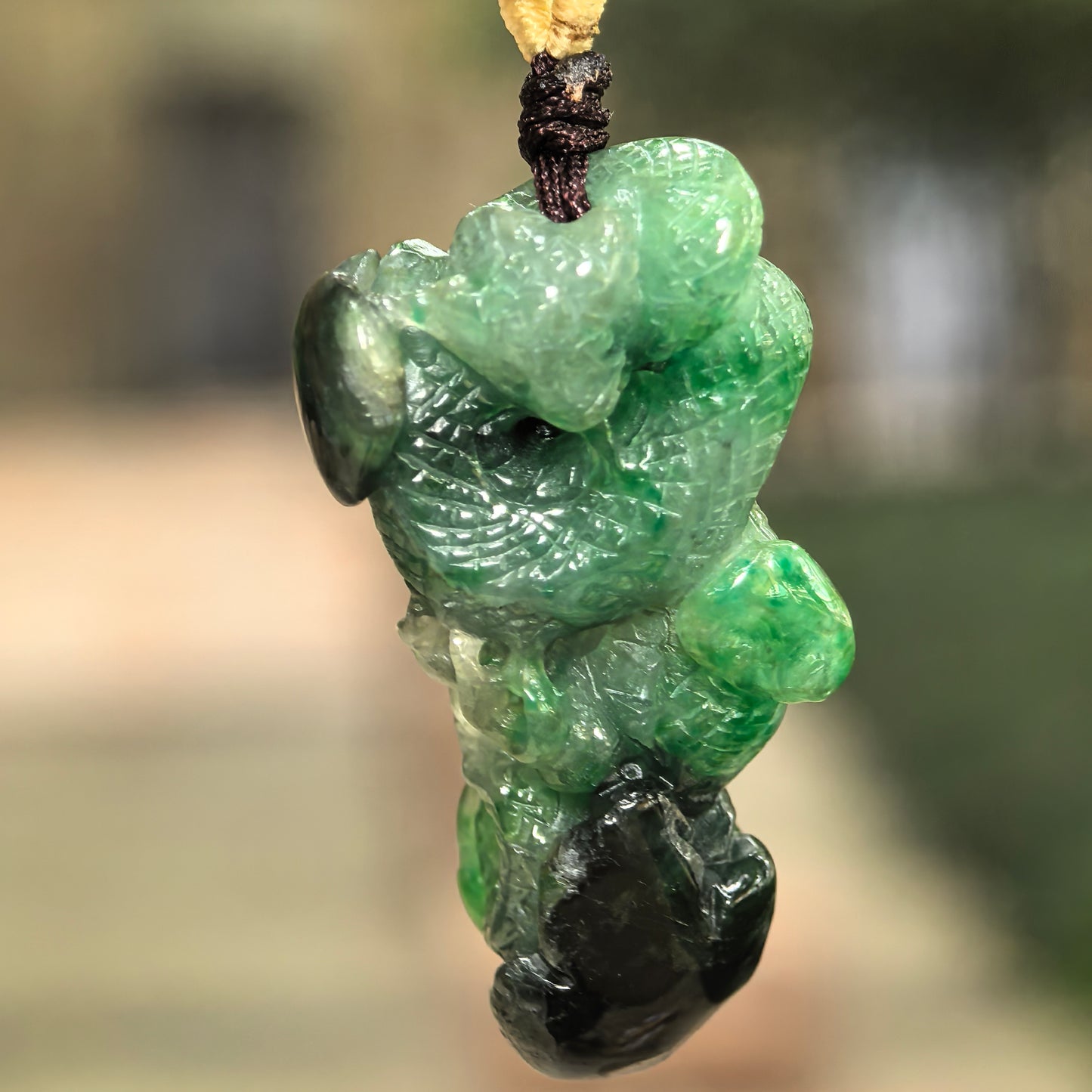 Natural Grade-A glutinous green and black jadeite snake pendant hanging on cord with bold color contrast.
