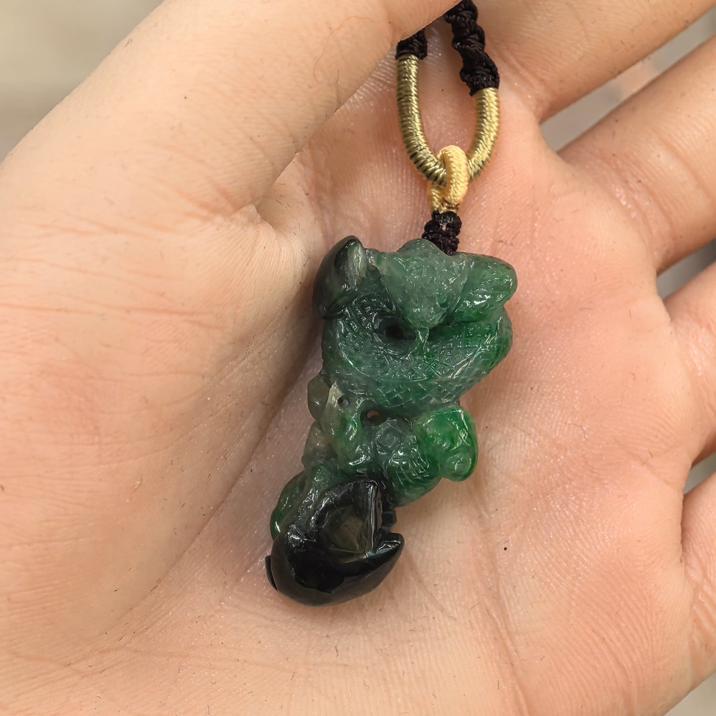 Three-dimensional carved jadeite snake pendant shown in hand with raised sculptural details.